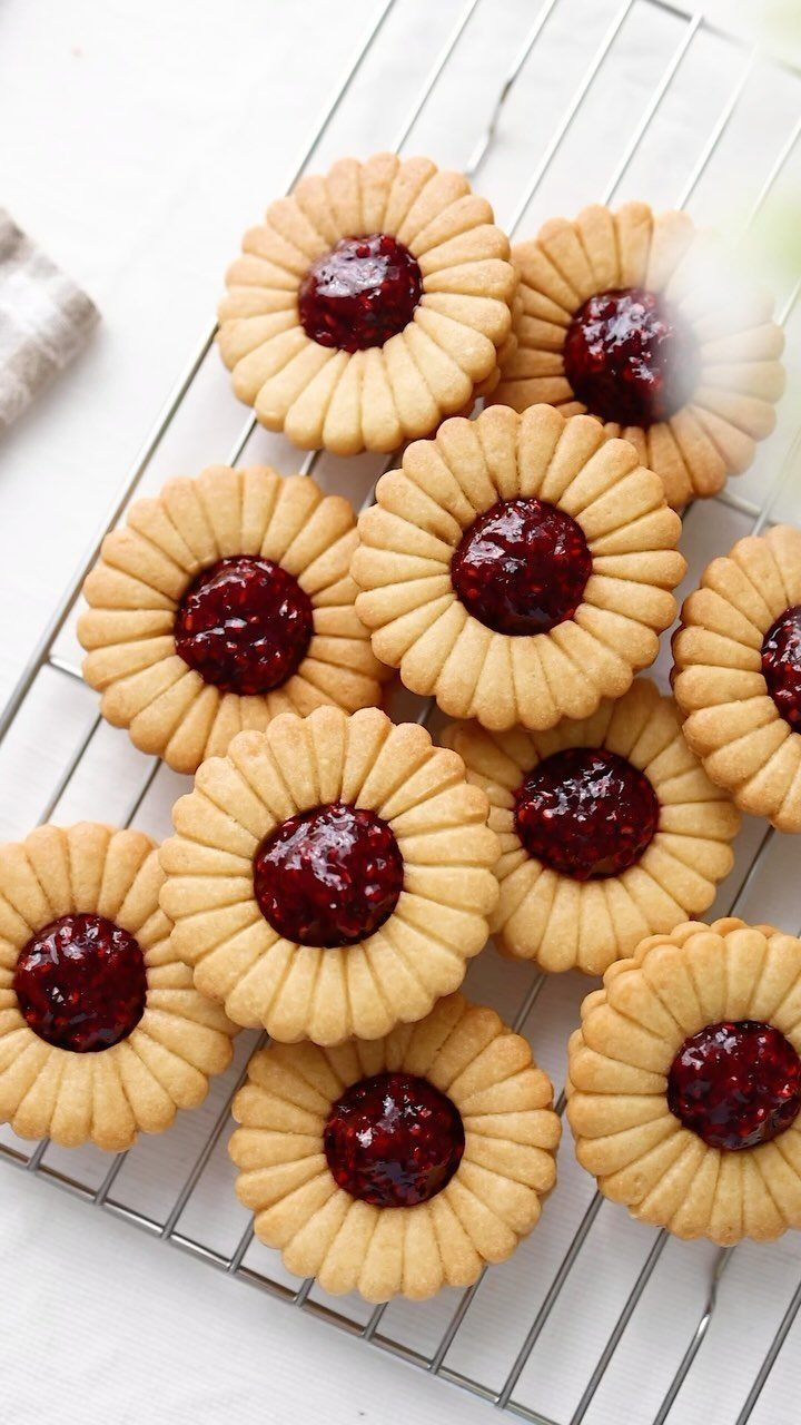 Flower-shaped shortbread cookies with red jam centers on a metal cooling rack.