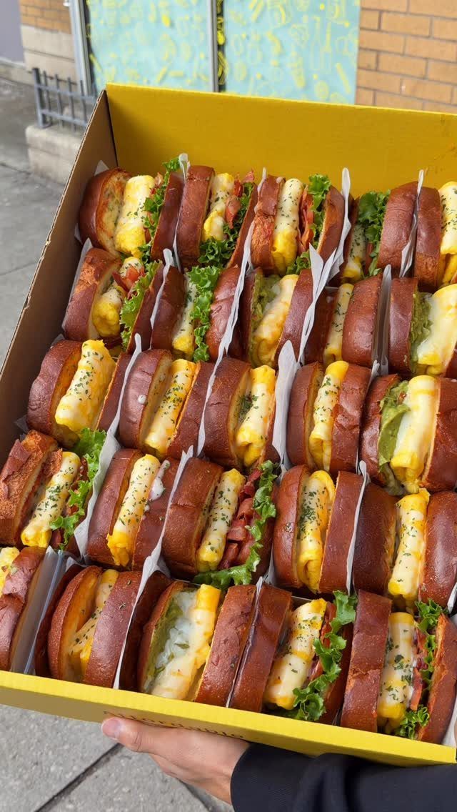Small sliders with yellow fillings and lettuce in a yellow cardboard box.