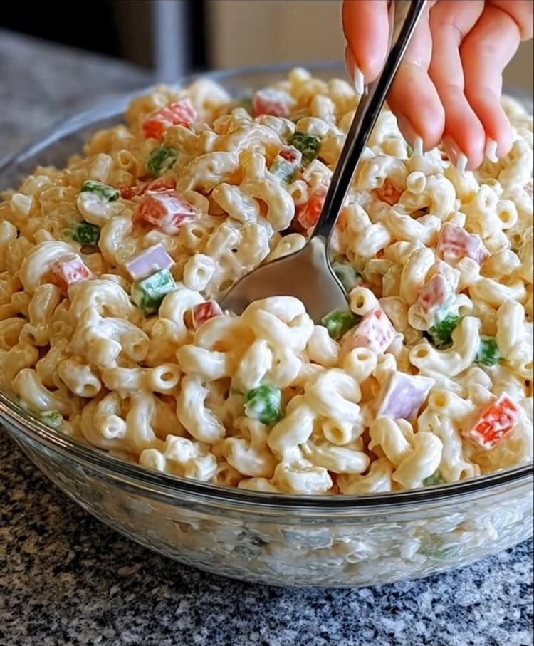 Macaroni pasta salad with colorful vegetables in a clear glass bowl being served.
