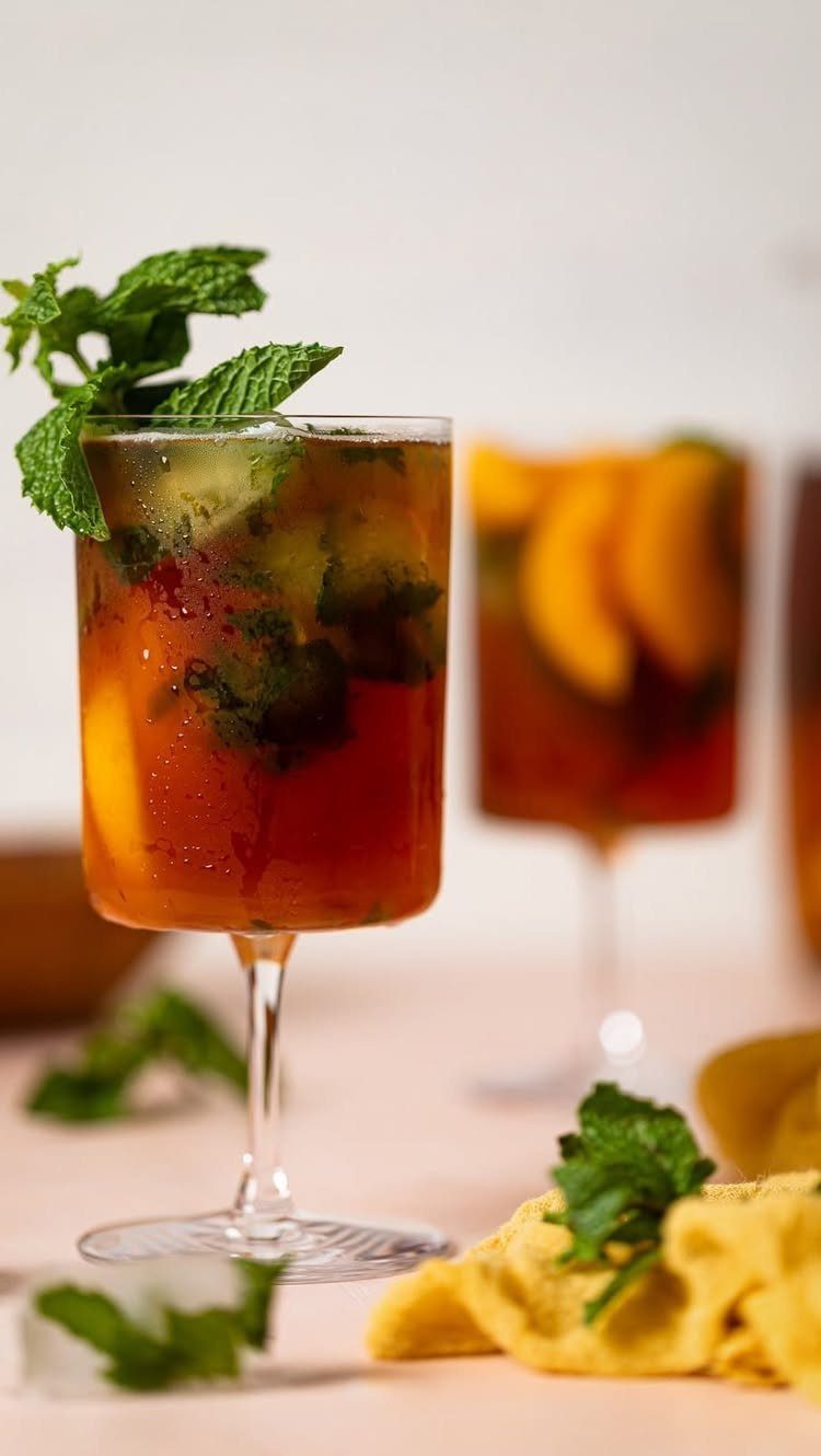 Iced tea in stemmed glasses garnished with fresh mint and peach slices.