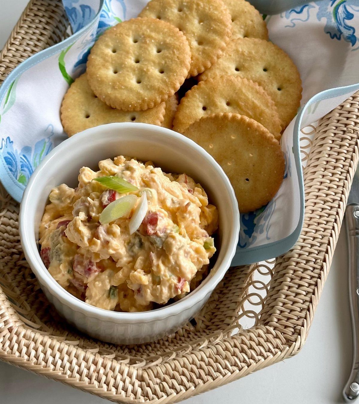 Pimento cheese spread in a white bowl served with round crackers in a basket.