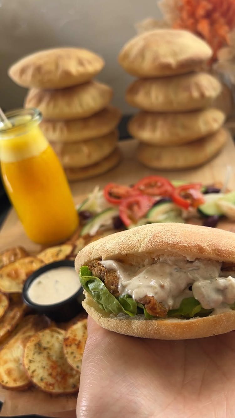 Pita bread sandwich with fried chicken and sauce, with stacks of pita bread behind.