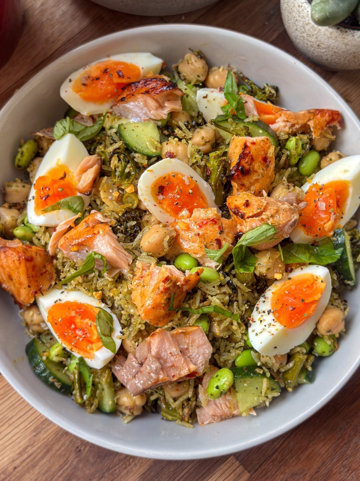 Rice salad with soft-boiled eggs, salmon, chickpeas, and greens in a white bowl.