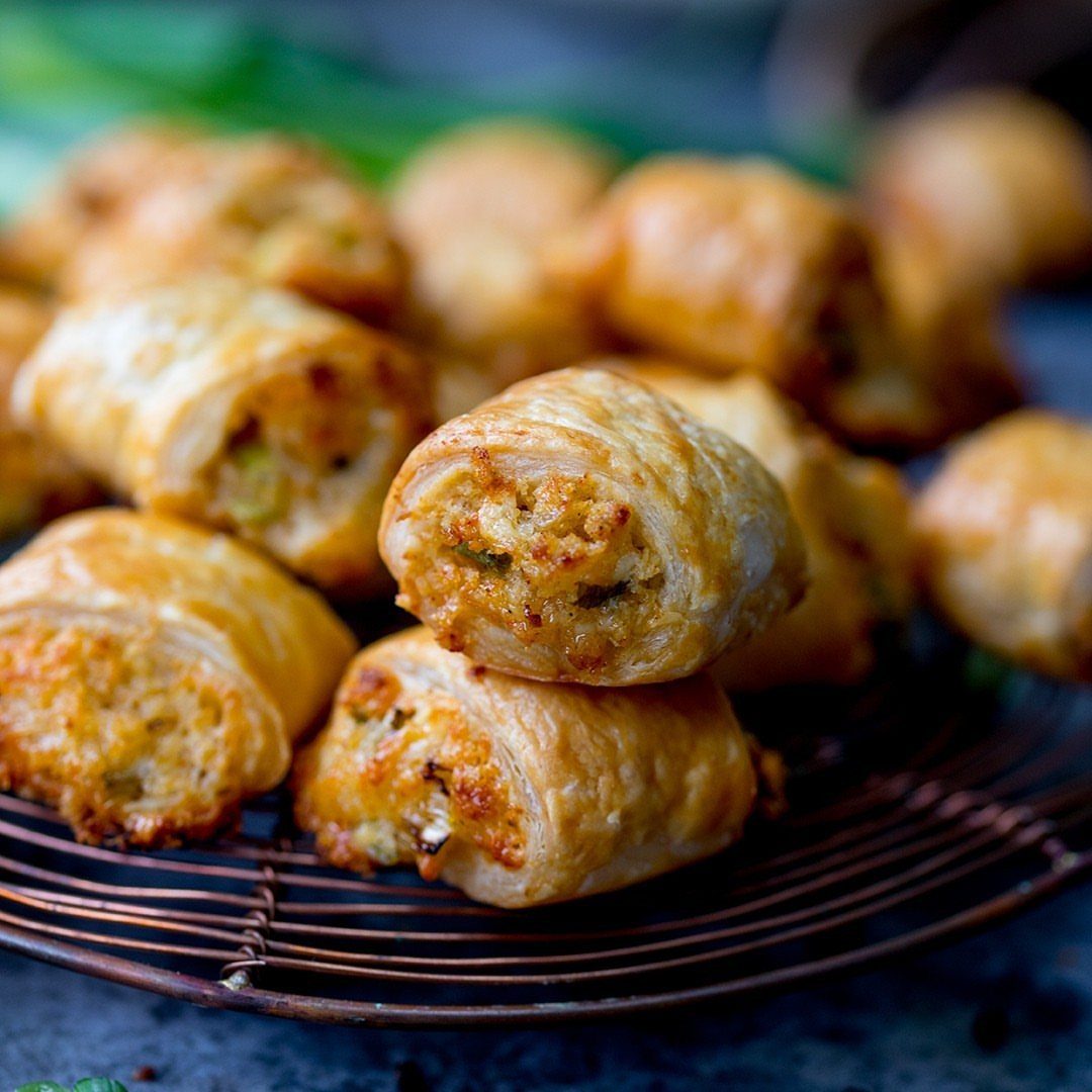 Golden-brown sausage rolls with flaky puff pastry on a wire cooling rack.