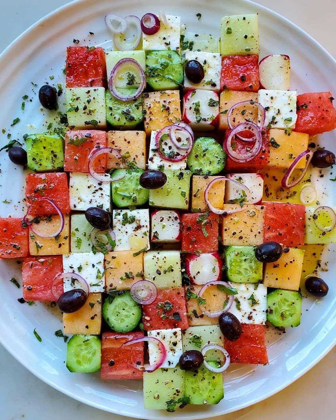 Watermelon salad with feta, cucumber, and olives arranged in a colorful grid pattern.