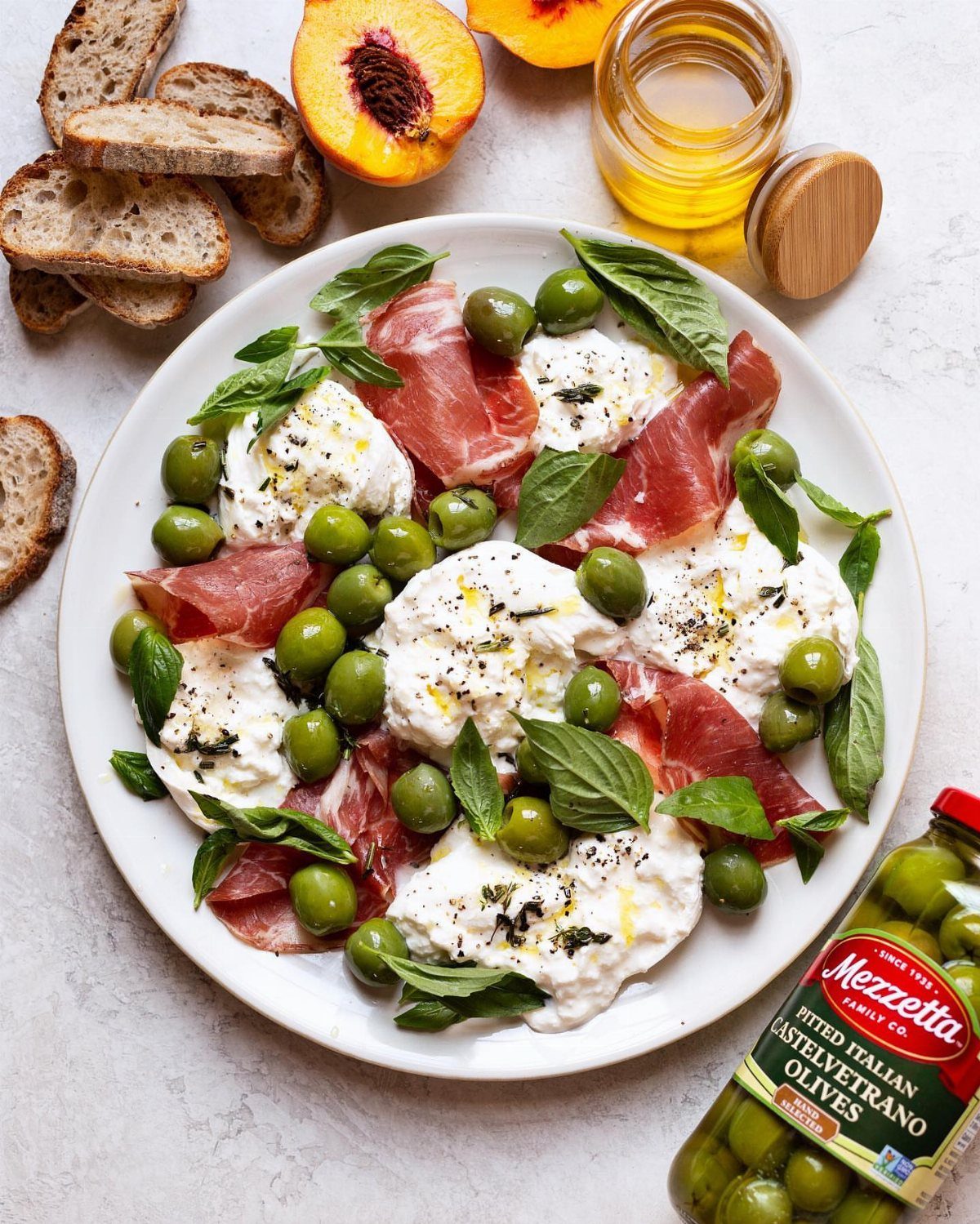 Burrata cheese, prosciutto, and green olives on a white plate with toasted bread.