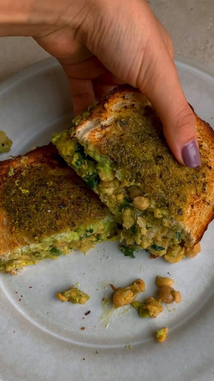 Toasted chickpea salad sandwich halves on a white plate held by a hand.