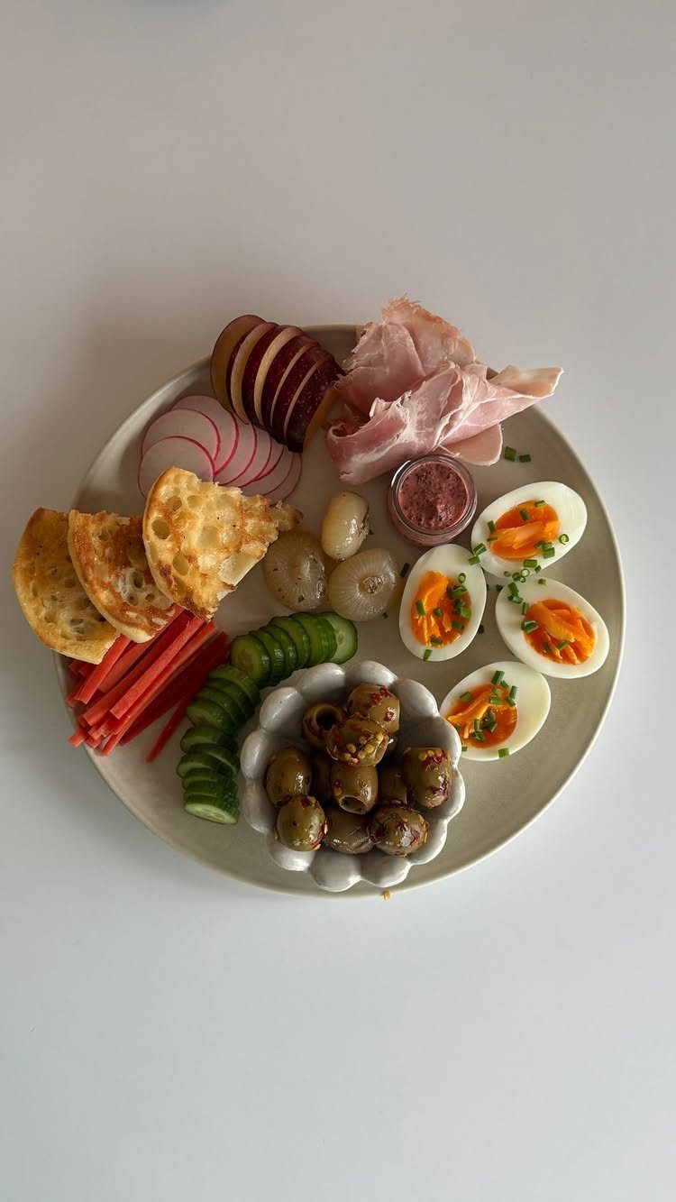 Assorted appetizer platter with eggs, olives, prosciutto, and vegetables on a white plate.