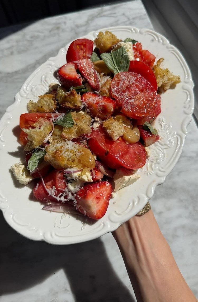 Strawberry and tomato salad with croutons and feta on a white scalloped platter.