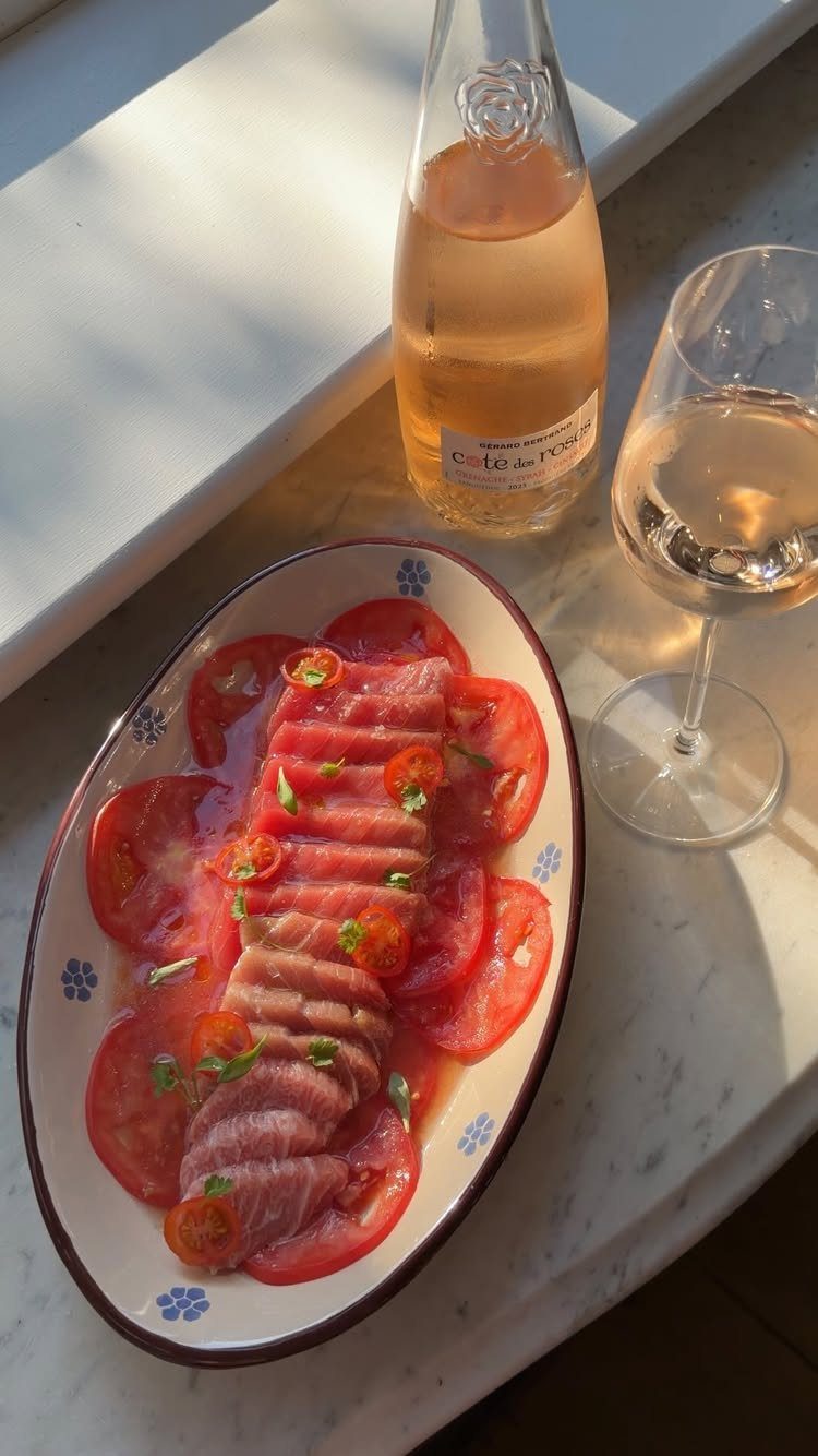 Thinly sliced raw tuna on tomato slices with a glass of rosé wine.