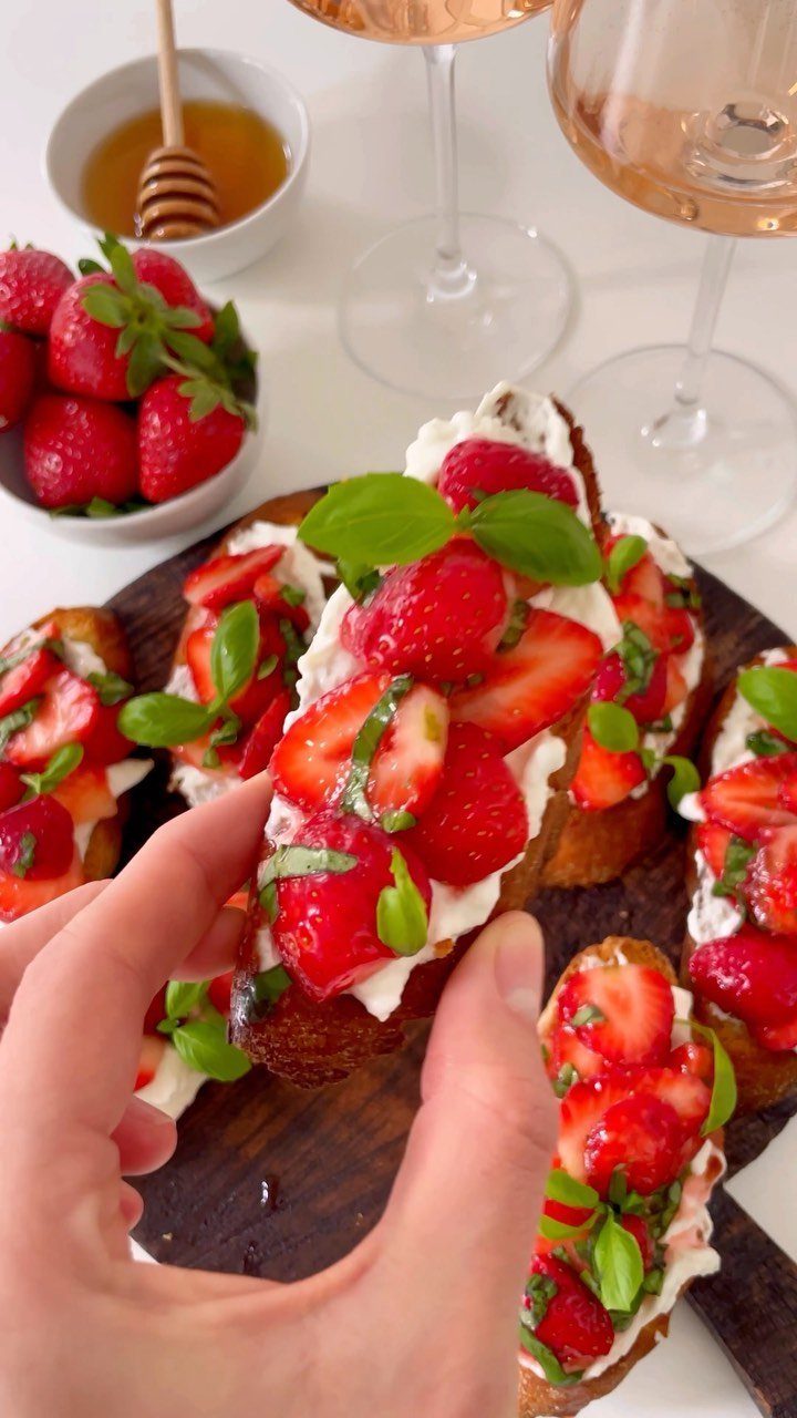 Strawberry bruschetta with cream cheese and basil on toasted bread held by a hand.