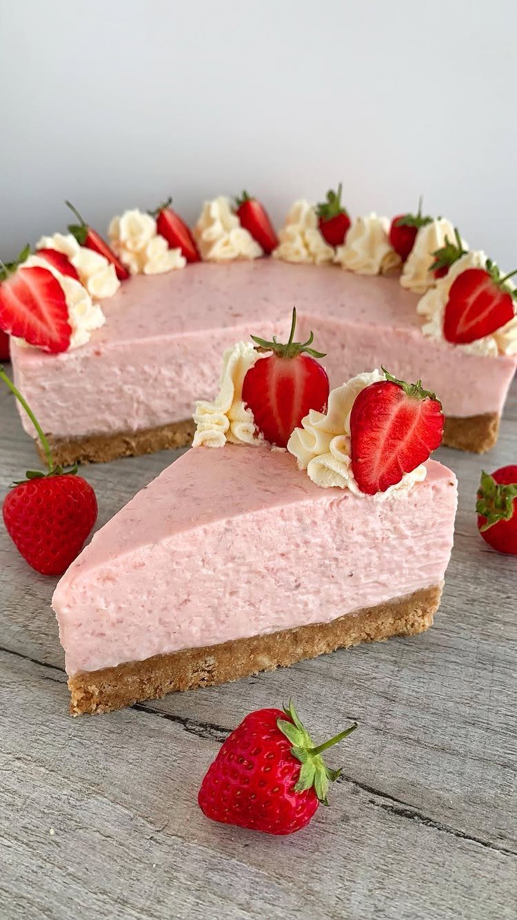 Pink strawberry cheesecake with whipped cream and fresh strawberries on a wooden table