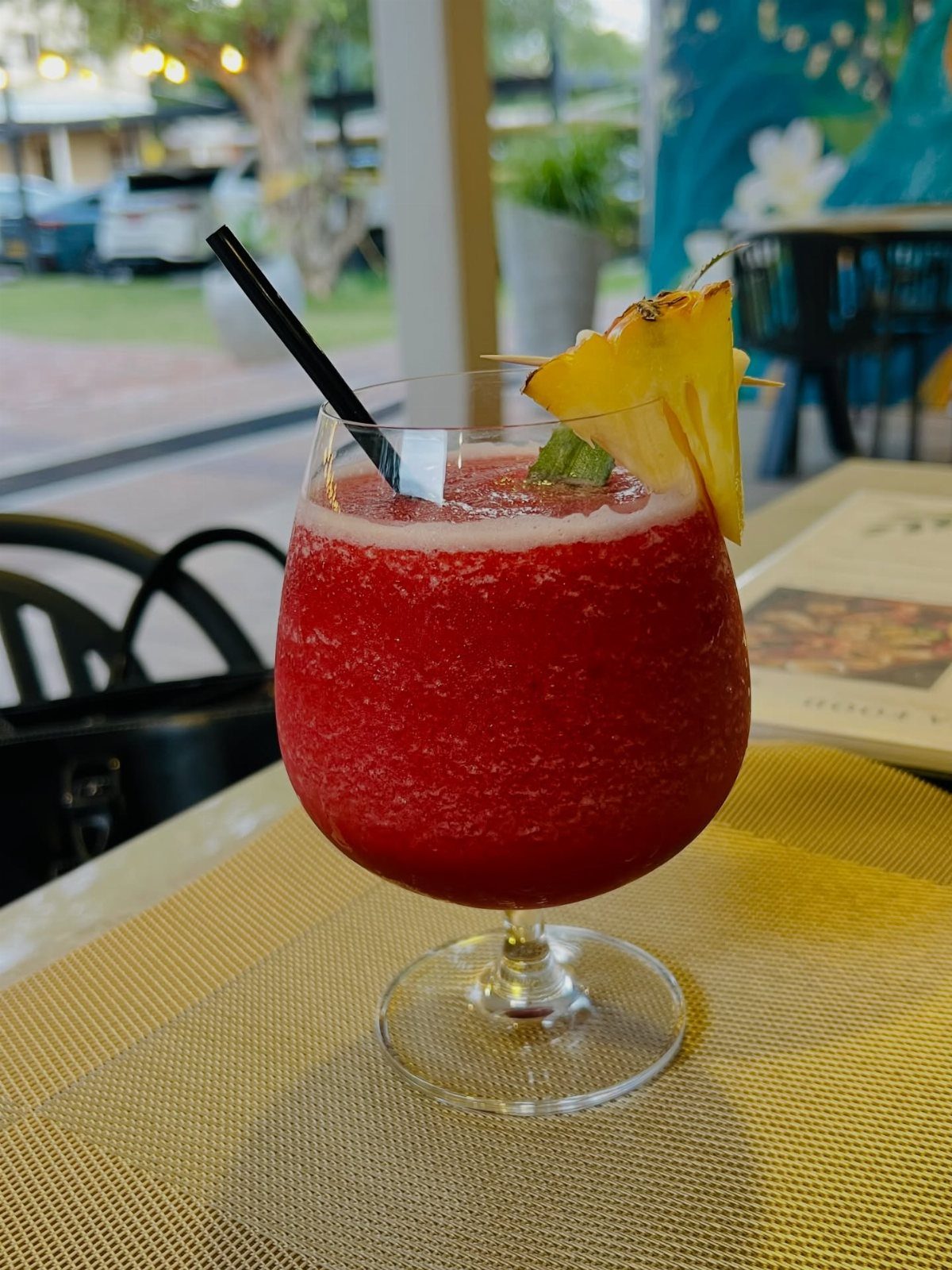 Frozen red strawberry drink in a glass with a pineapple slice and mint leaf.
