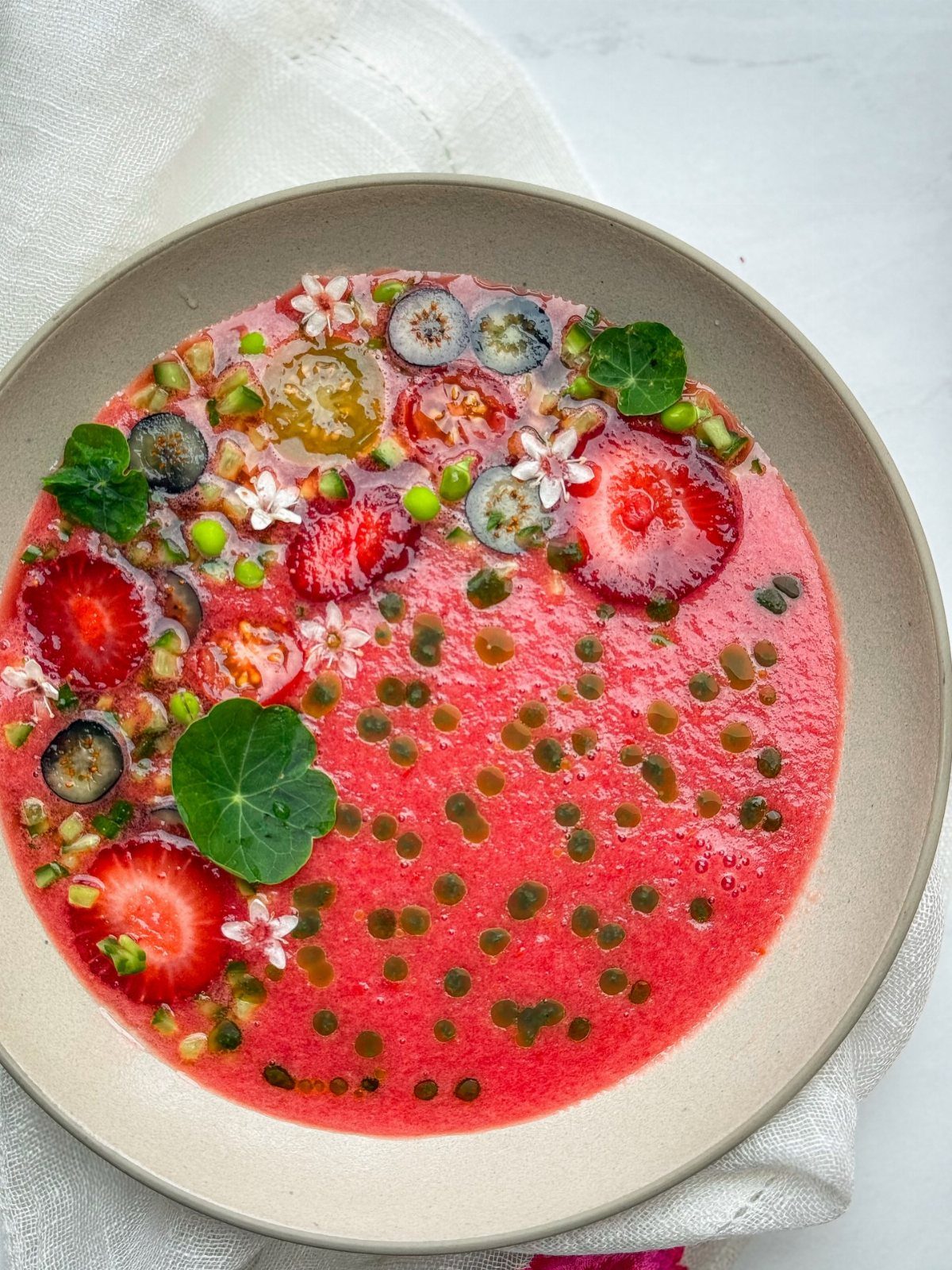 Strawberry gazpacho in a bowl topped with berries, peas, and fresh herbs.