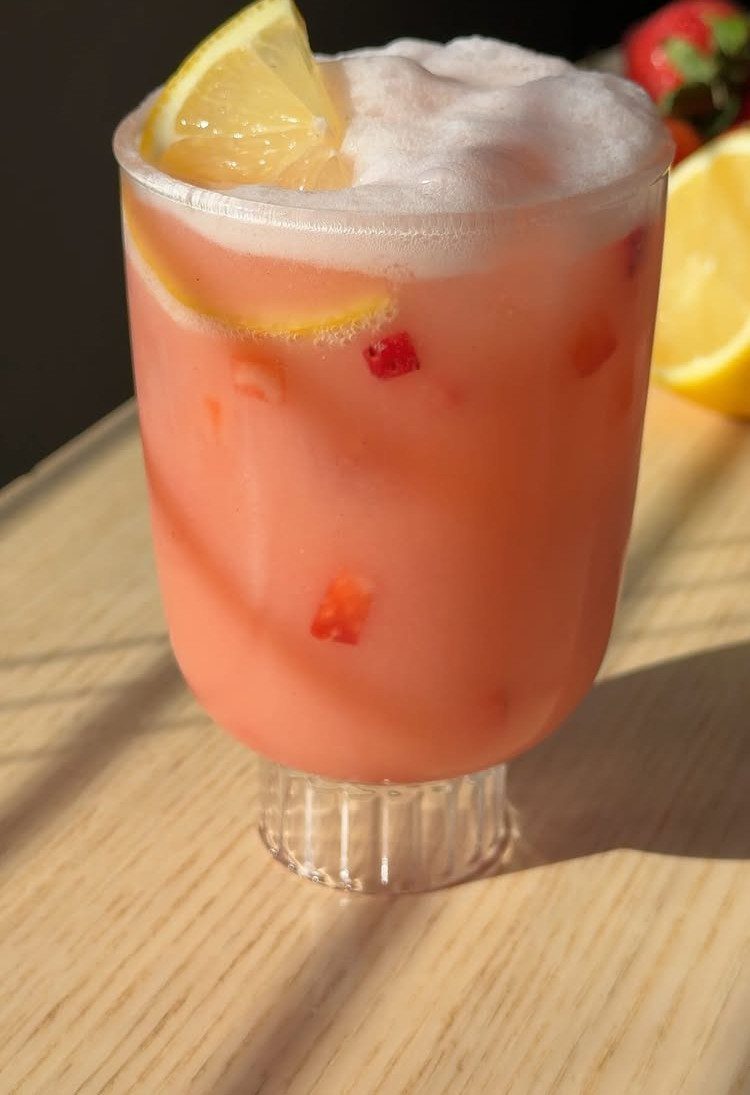 Pink strawberry lemonade in a glass with foam and a lemon wedge garnish.