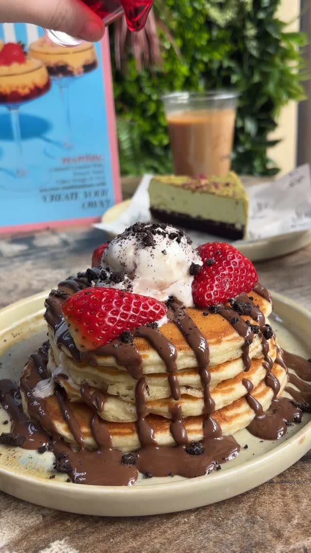 Stack of pancakes topped with fresh strawberries, vanilla ice cream, and chocolate drizzle.