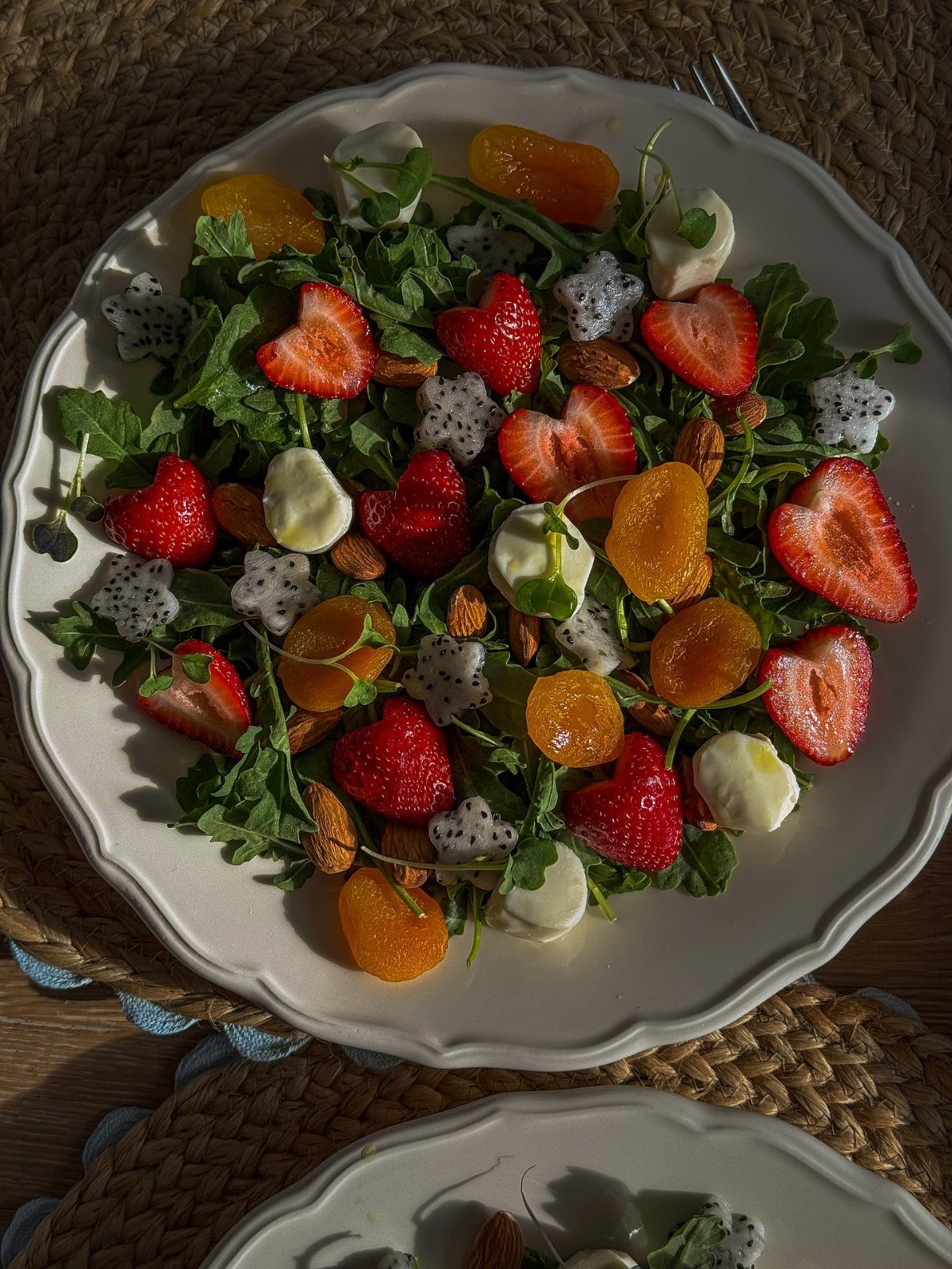 Strawberry salad with mozzarella, almonds, dragon fruit, and apricots on a white plate.