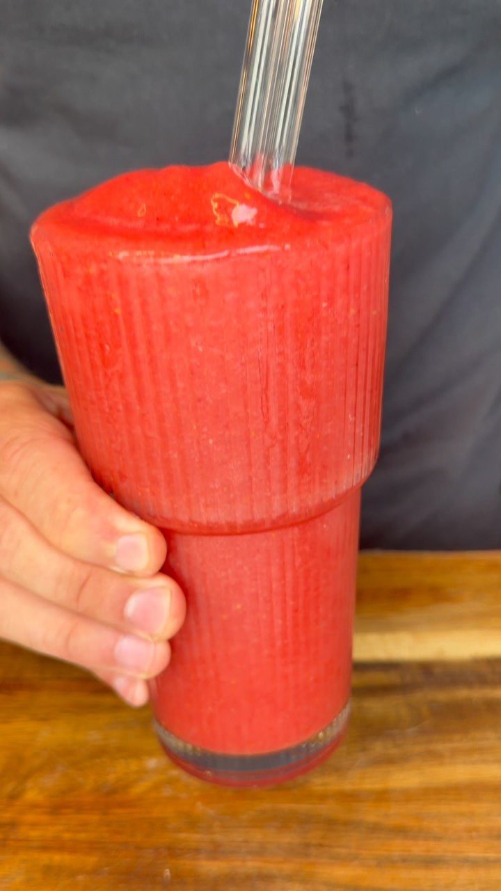 Frozen red strawberry slushie in a ribbed glass with a clear straw.