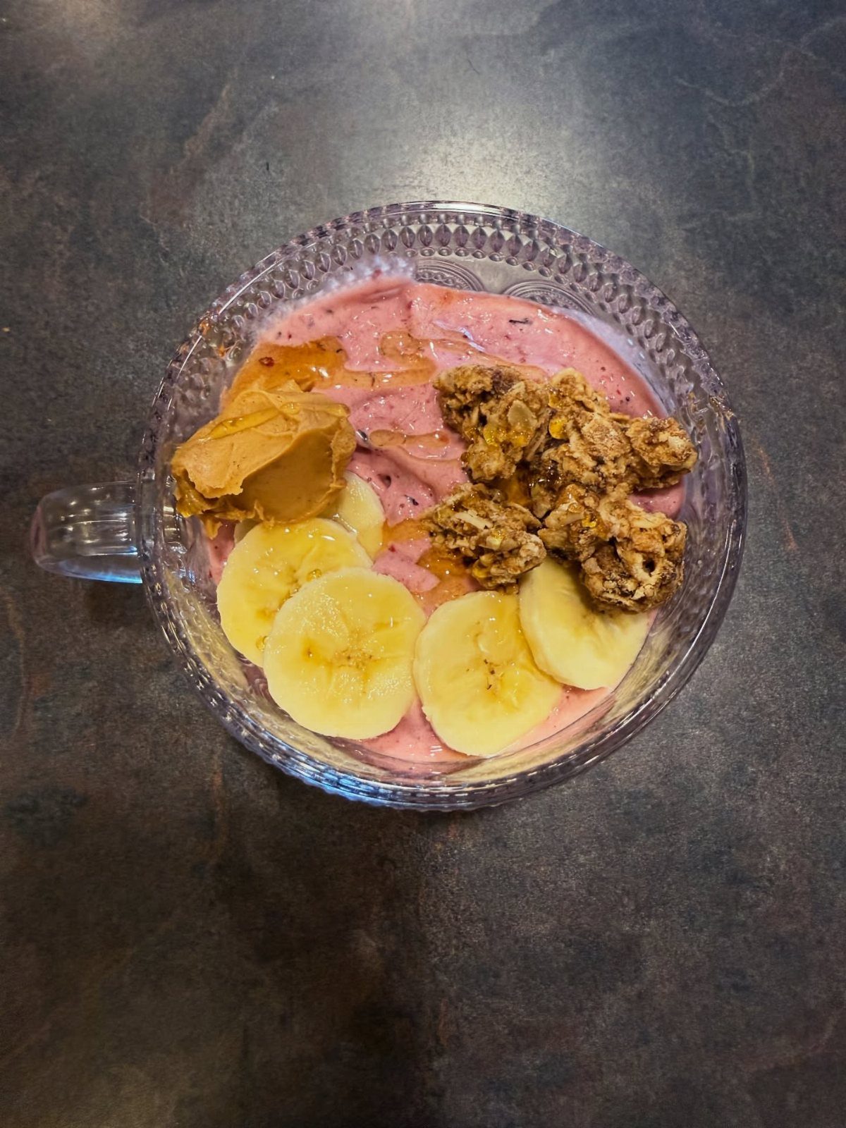 Strawberry smoothie bowl topped with banana slices, granola, and peanut butter.