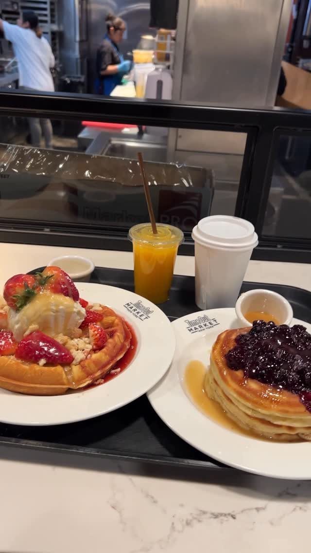 Waffle with strawberries and ice cream next to blueberry pancakes on a tray.