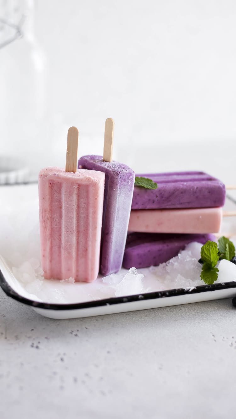 Pink and purple frozen popsicles on a tray of crushed ice with mint leaves.