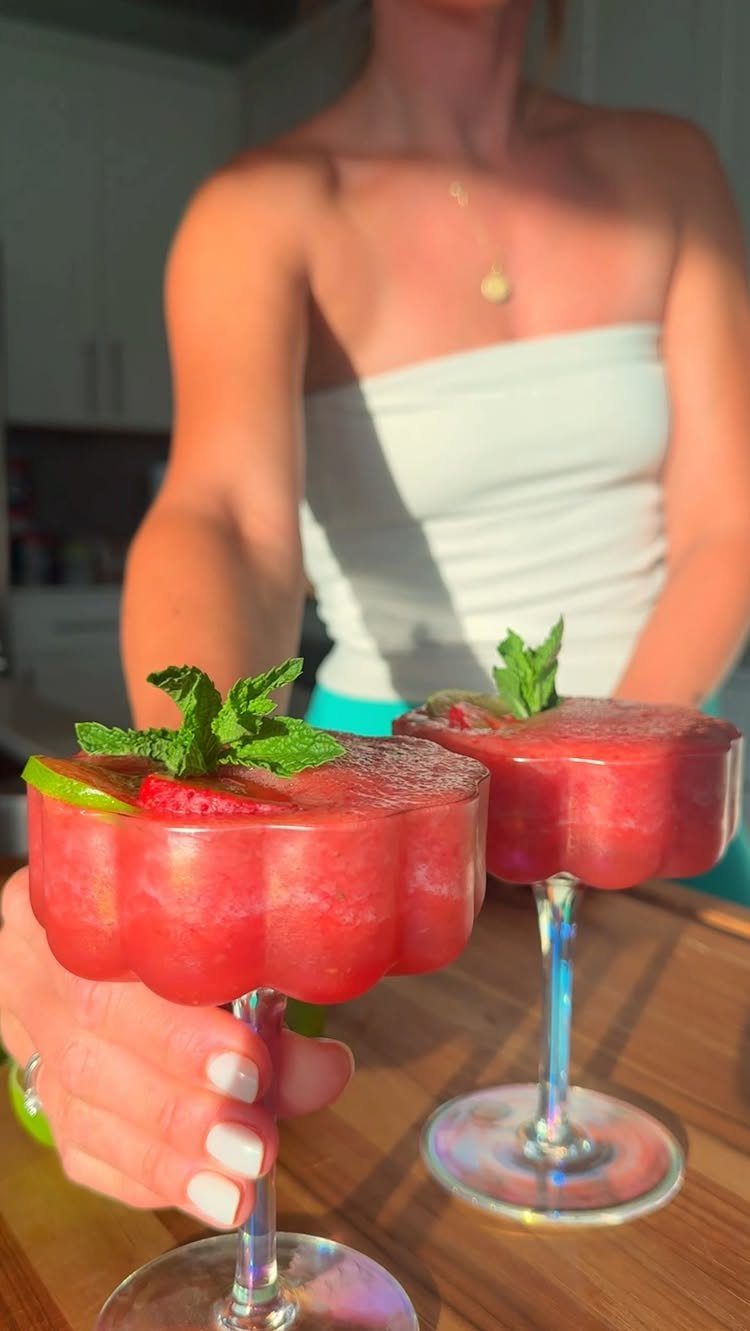 Red frozen mocktails with mint, strawberries, and lime in scalloped glasses.