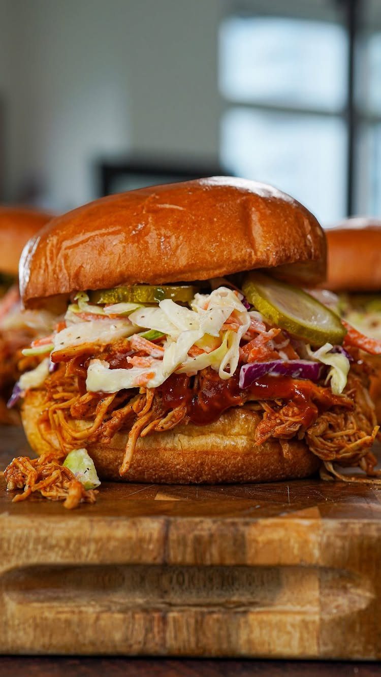 BBQ pulled chicken sandwich with coleslaw and pickles on a wooden board