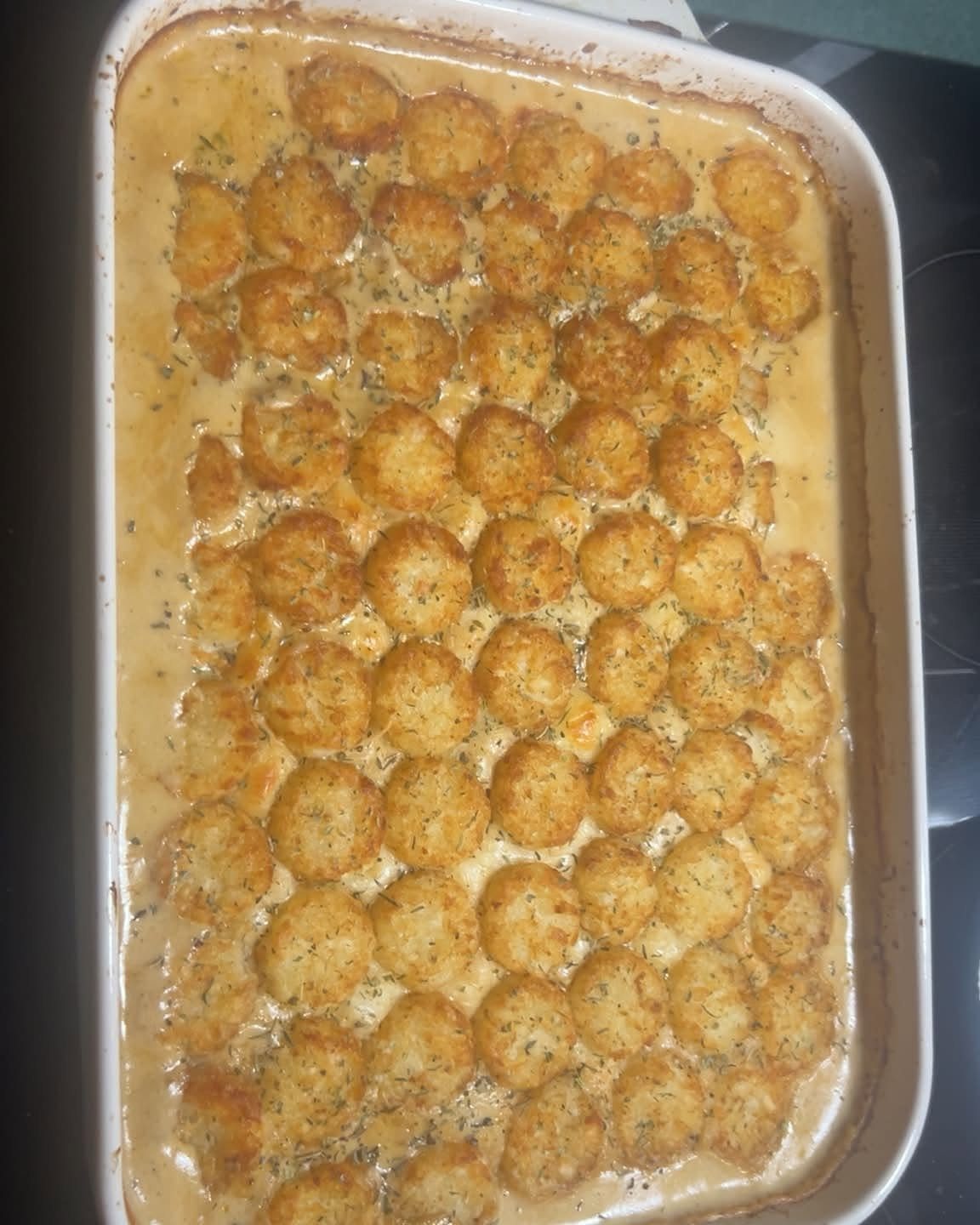 Cheesy chicken casserole topped with golden-brown tater tots in a white baking dish.