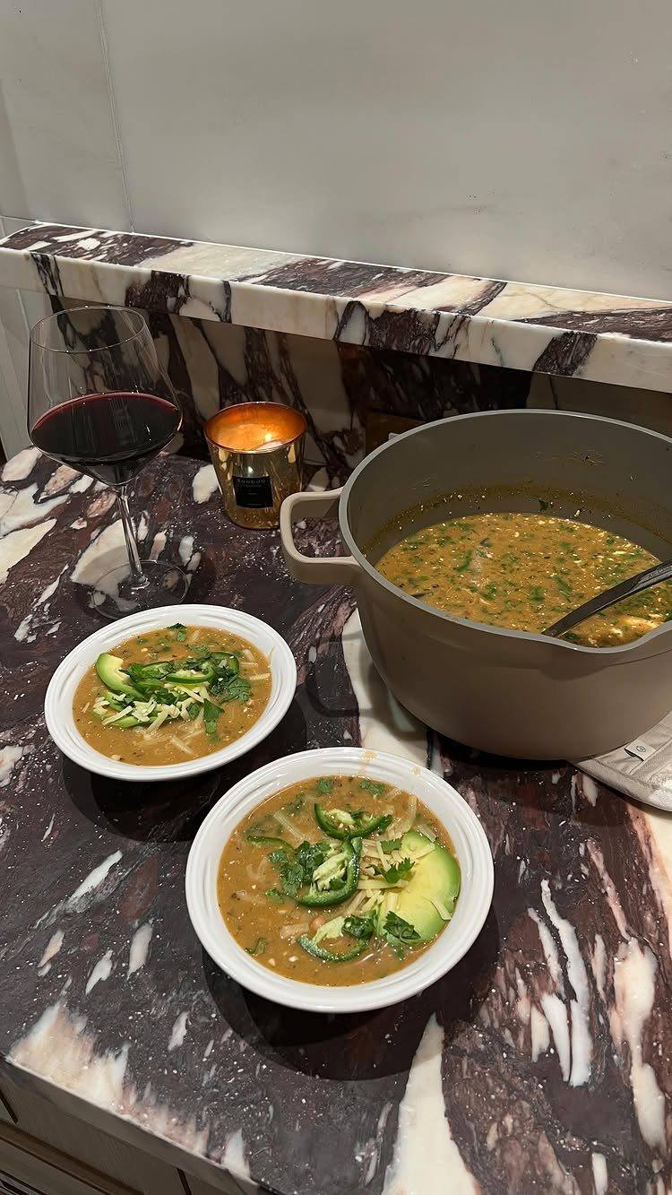 Chicken chili in bowls and a pot with avocado slices on a marble counter.