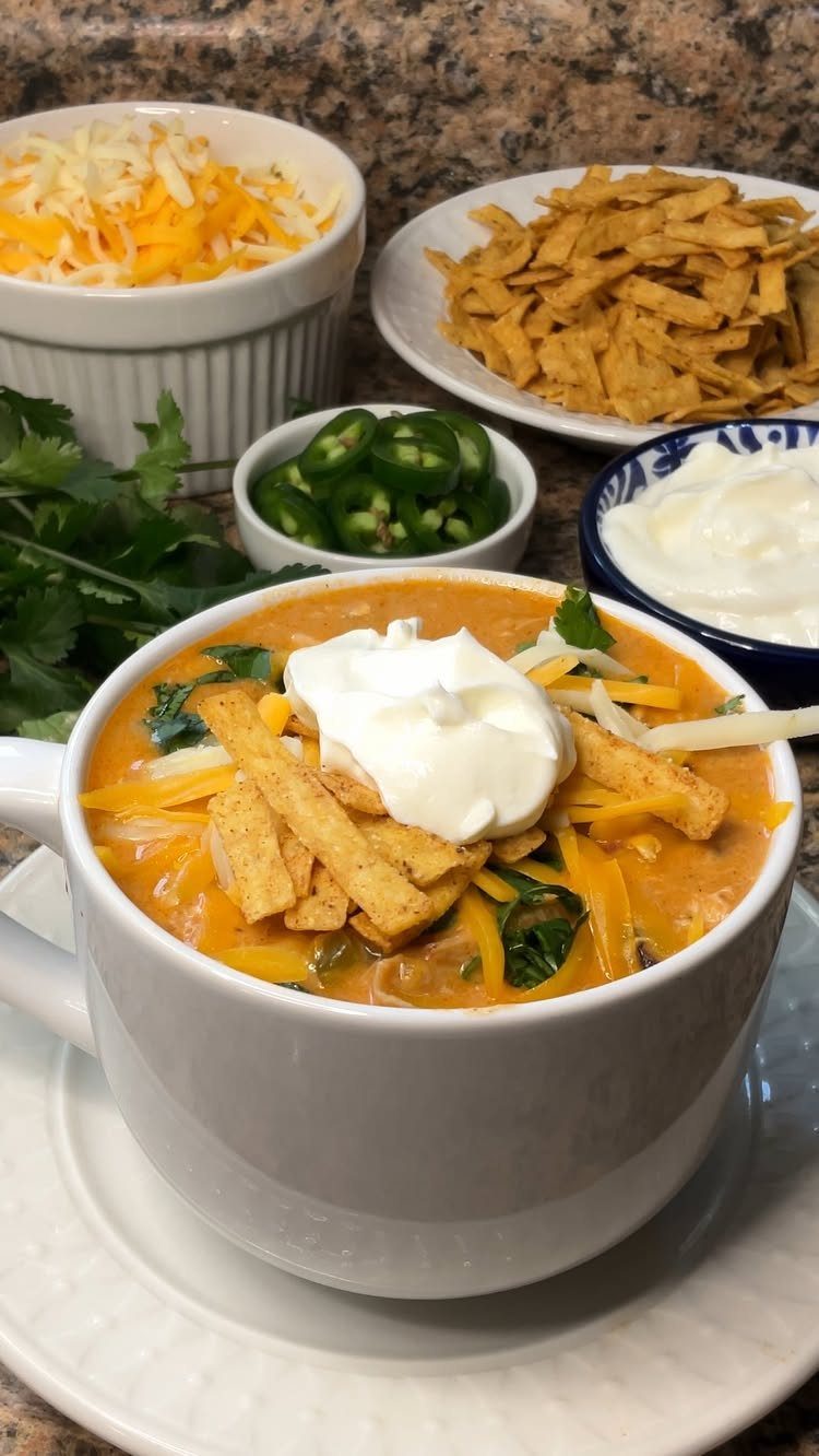 Chicken enchilada soup in a white bowl topped with sour cream and tortilla strips.