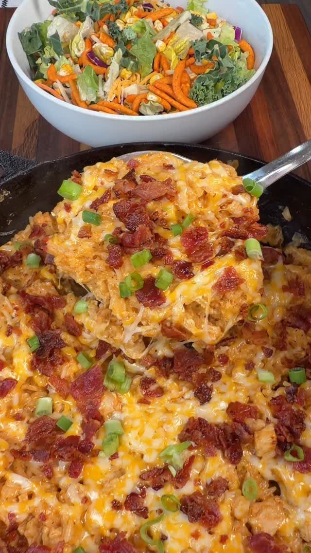 Creamy chicken with melted cheddar, bacon, and green onions in a black skillet.
