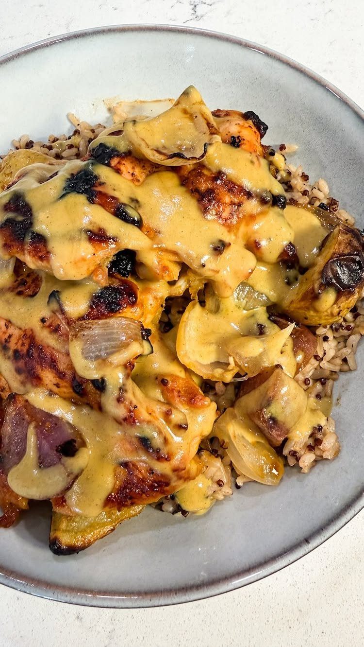 Cooked chicken with creamy yellow sauce, mushrooms, and onions over brown rice.