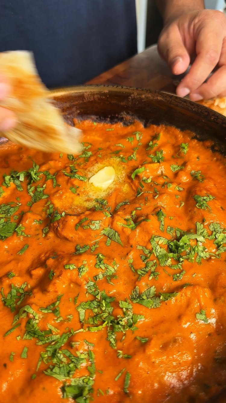 Butter chicken in a pot topped with melting butter and fresh cilantro herbs.