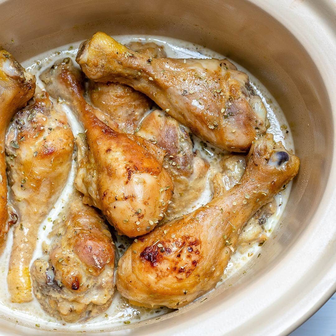 Chicken drumsticks in a creamy herb sauce inside a ceramic slow cooker pot.
