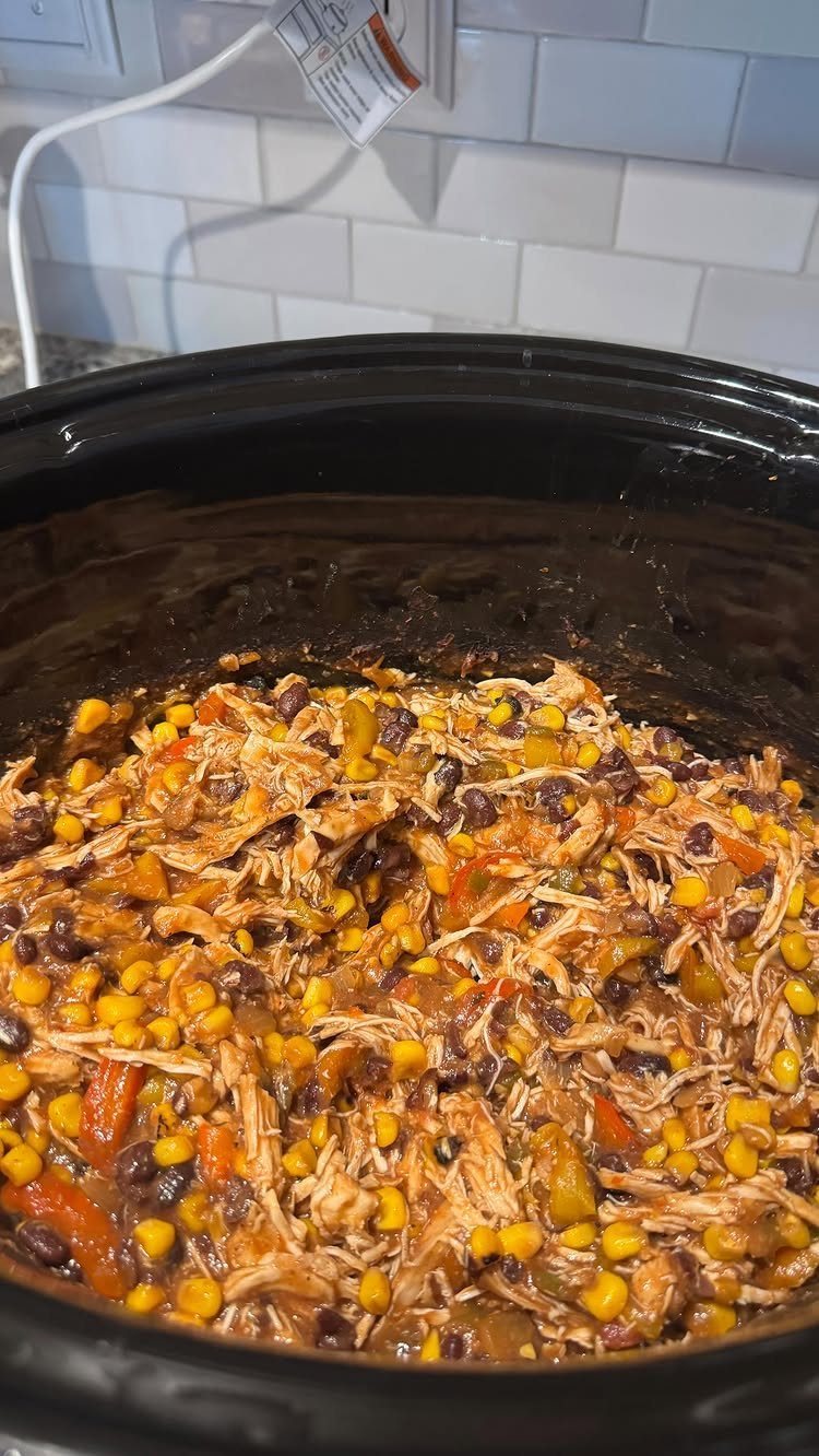 Shredded chicken with corn and black beans inside a black slow cooker pot.