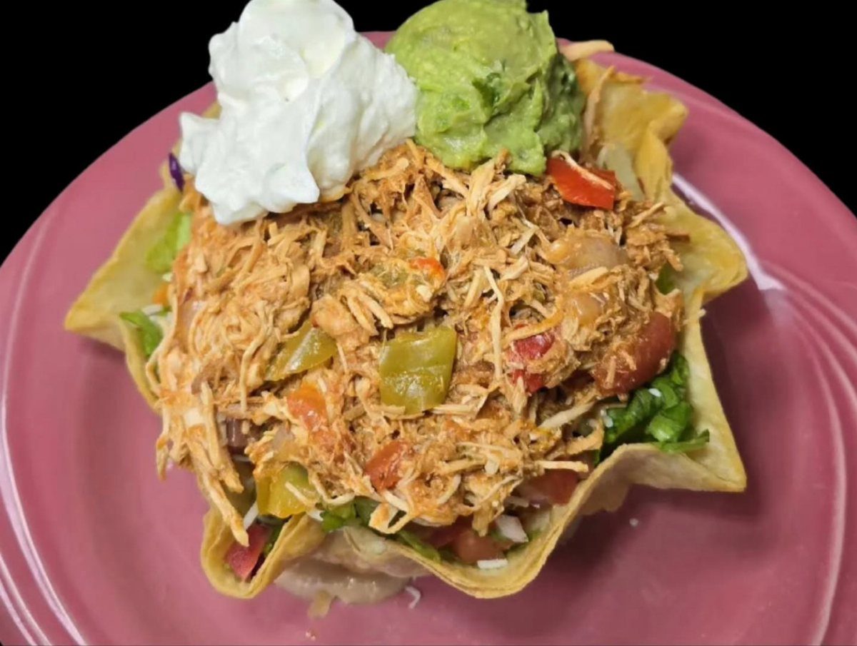 Shredded taco chicken in a tortilla bowl with guacamole and sour cream.
