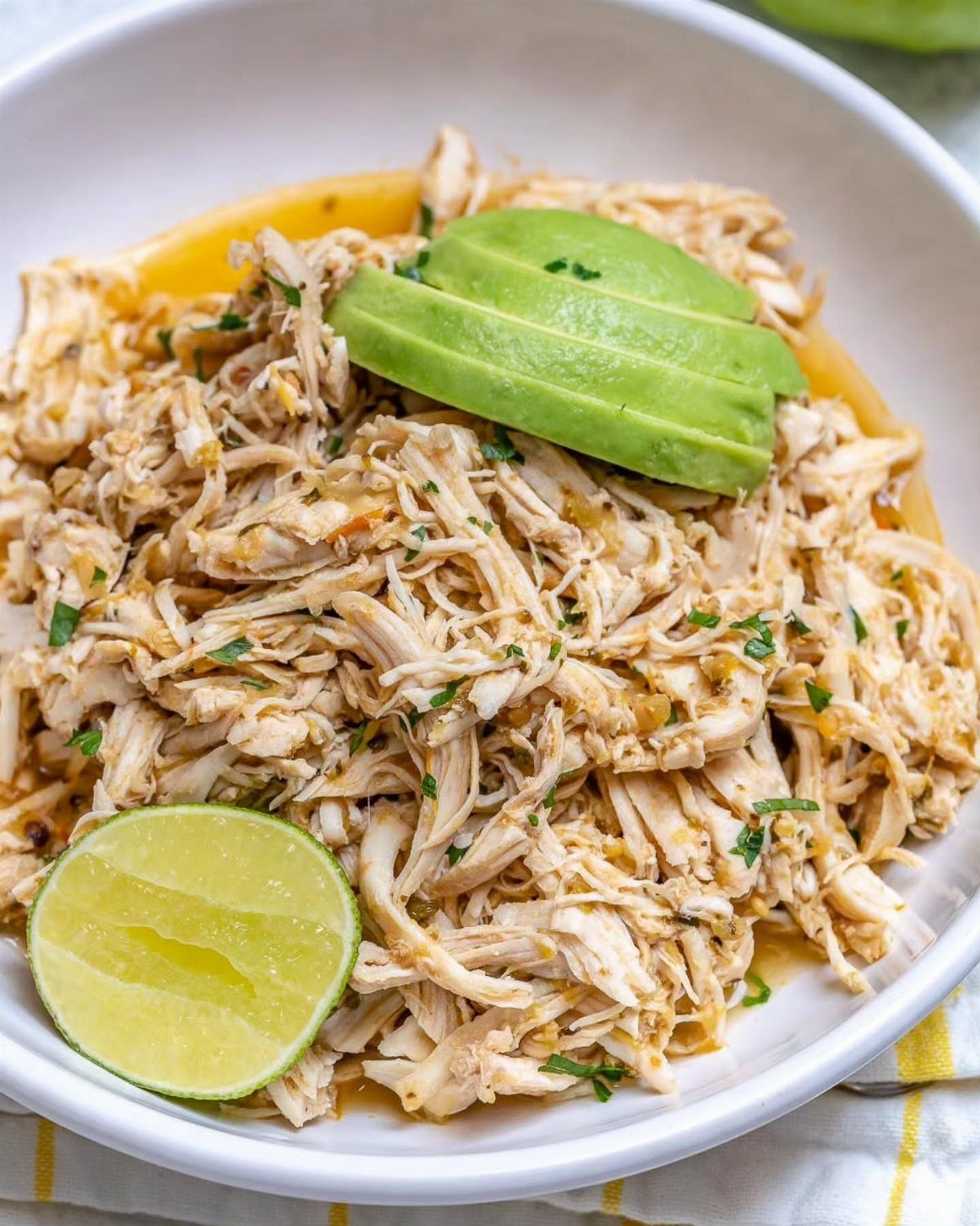 Shredded taco chicken in a white bowl topped with avocado slices and lime.