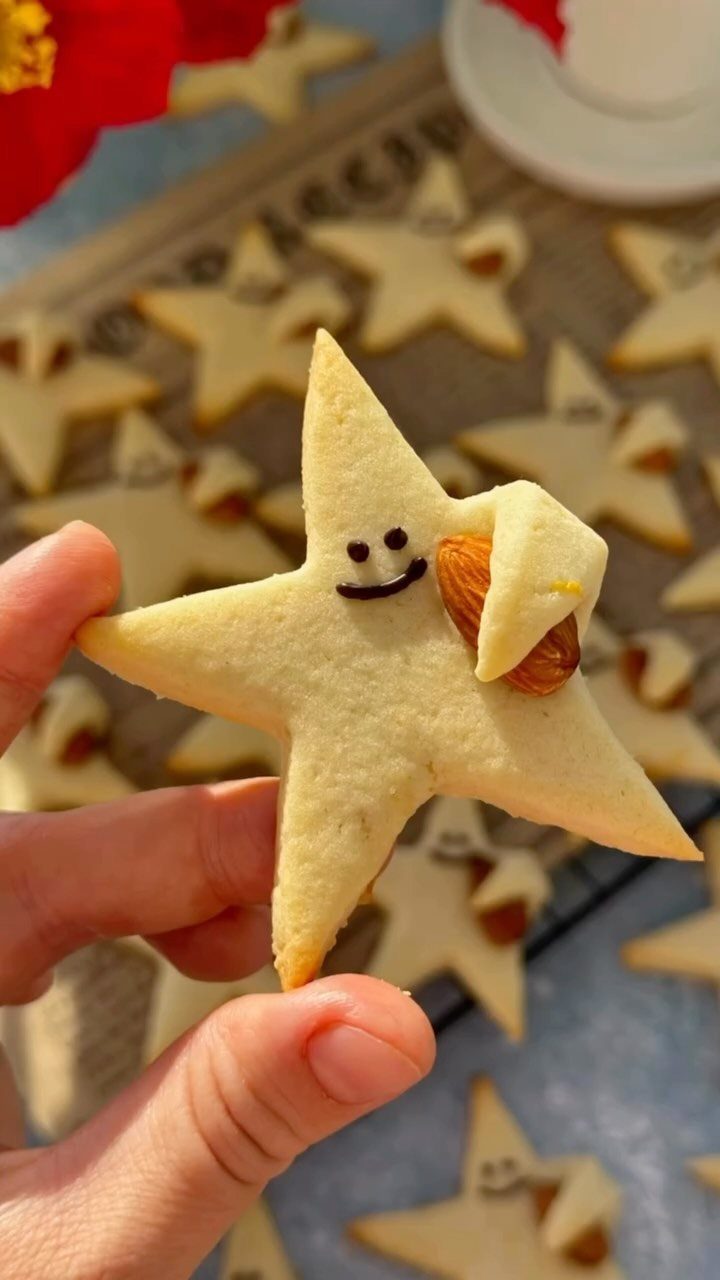 Fun Shaped Cookies: 35 Cut-Out Cookie Recipes to Decorate 12 Star-shaped cookie with a smiling face and a whole almond decoration held by hand.