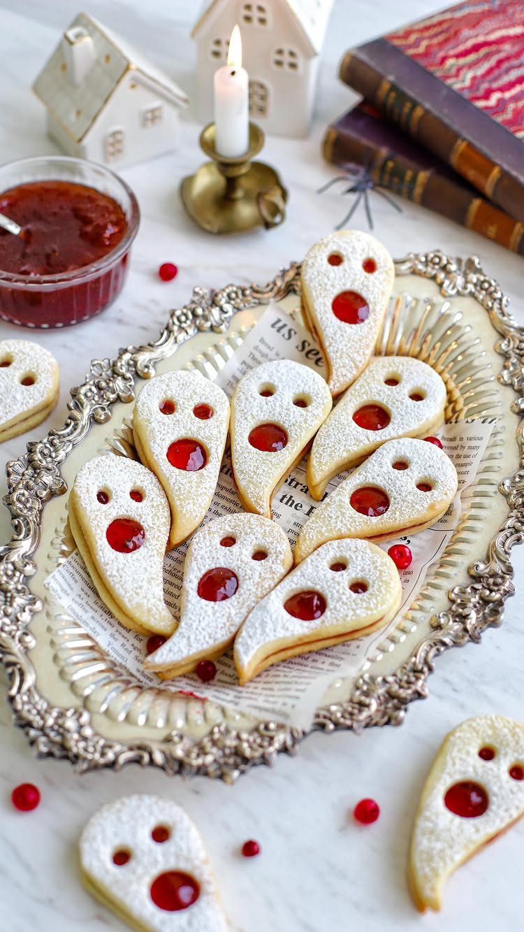 Fun Shaped Cookies: 35 Cut-Out Cookie Recipes to Decorate 8 Ghost-shaped cookies with white icing and red jam centers on a silver platter.