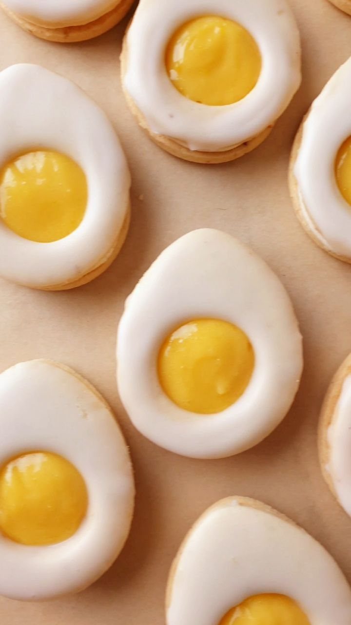 Fun Shaped Cookies: 35 Cut-Out Cookie Recipes to Decorate 28 Egg-shaped cookies with white icing and yellow centers resembling fried eggs on parchment paper.