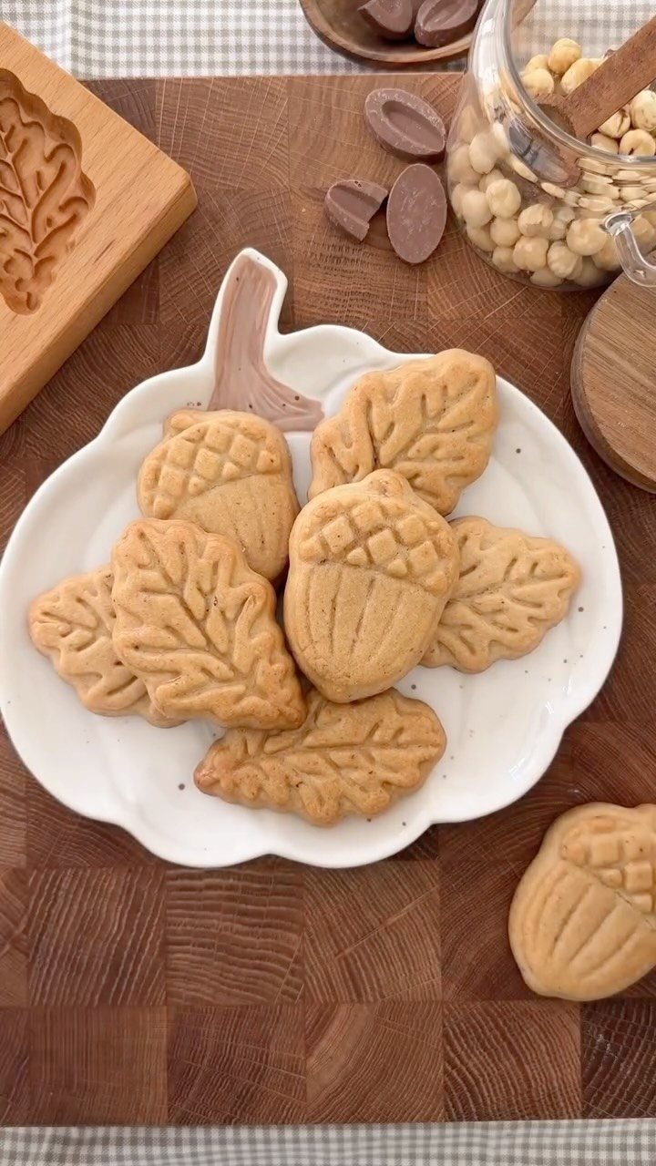 Fun Shaped Cookies: 35 Cut-Out Cookie Recipes to Decorate 13 Acorn and leaf shaped cookies on a white plate with hazelnuts nearby.