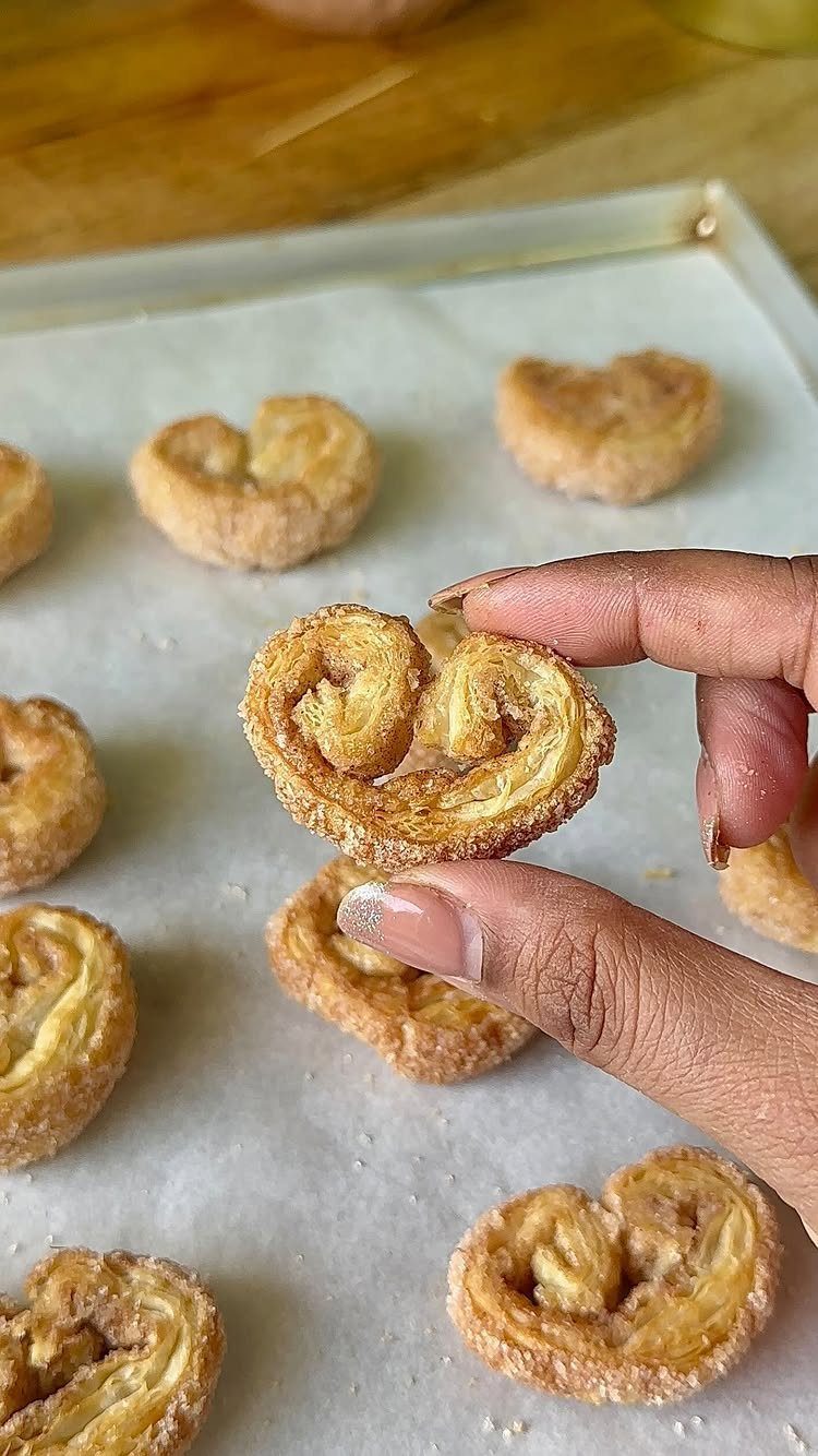 Fun Shaped Cookies: 35 Cut-Out Cookie Recipes to Decorate 31 Heart-shaped cinnamon sugar pastries on a parchment-lined baking sheet held by a hand.