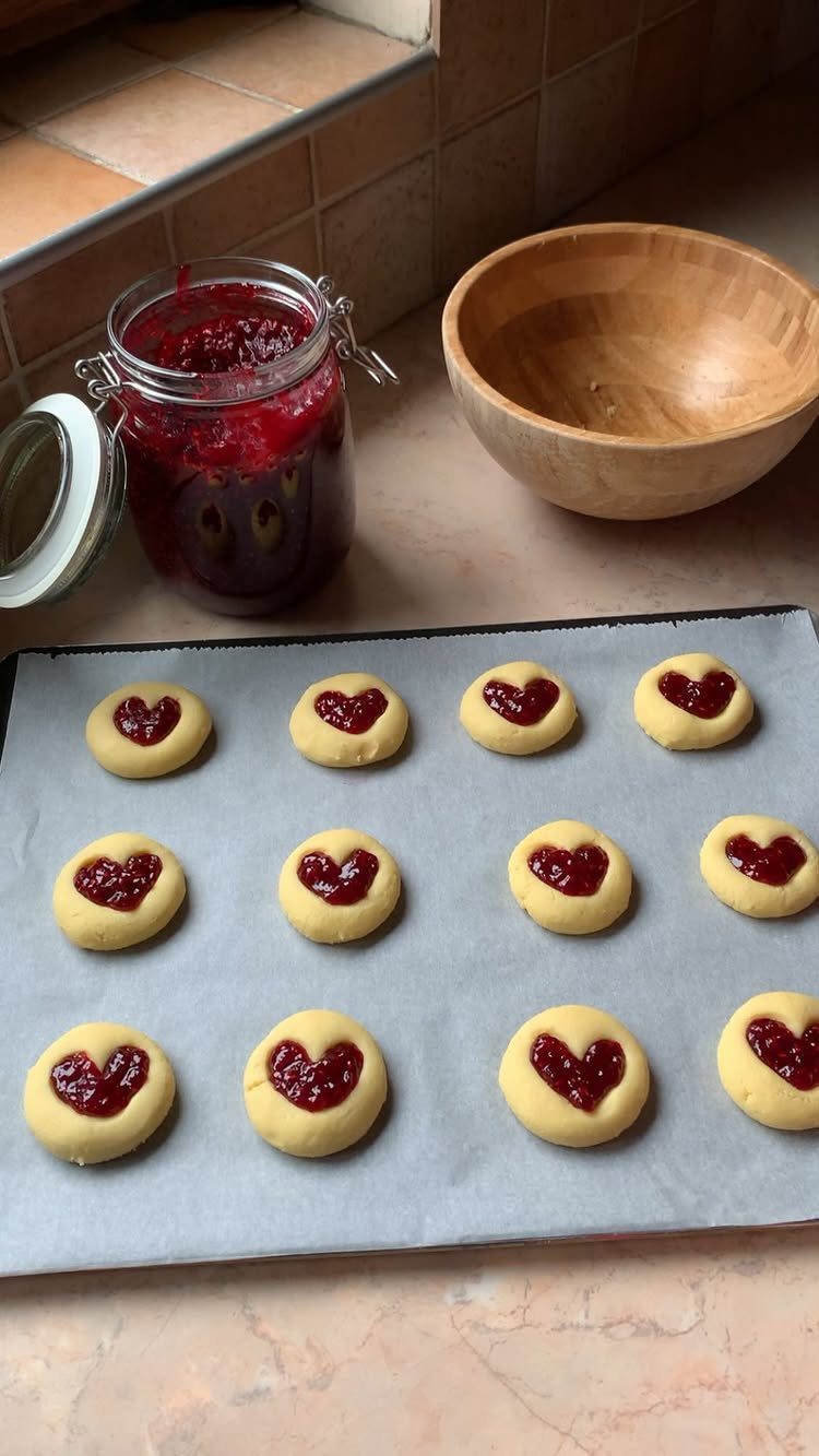 Fun Shaped Cookies: 35 Cut-Out Cookie Recipes to Decorate 35 Heart-shaped jam filled sugar cookies on a baking sheet next to a jam jar.