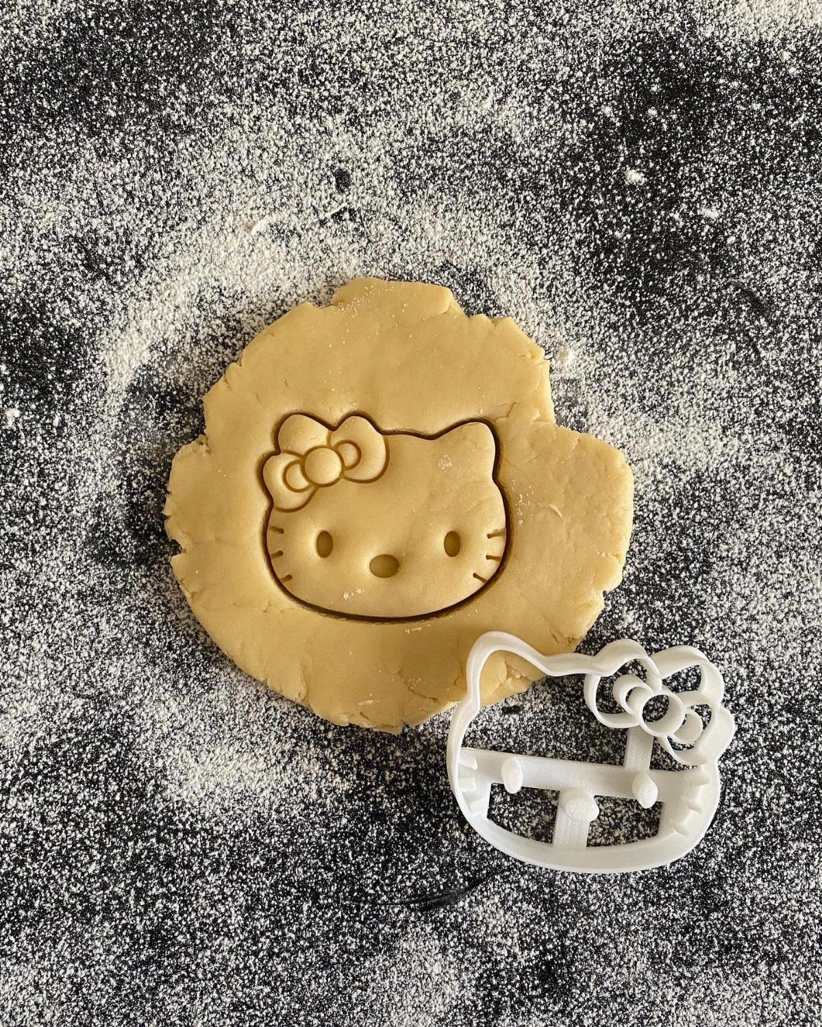 Fun Shaped Cookies: 35 Cut-Out Cookie Recipes to Decorate 36 Hello Kitty shaped cookie dough and white plastic cutter on floured dark surface