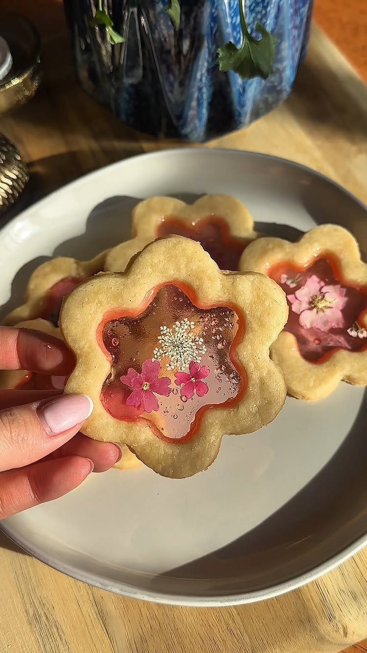 Fun Shaped Cookies: 35 Cut-Out Cookie Recipes to Decorate 20 Flower-shaped cookies with translucent red candy centers and edible flowers on a plate.