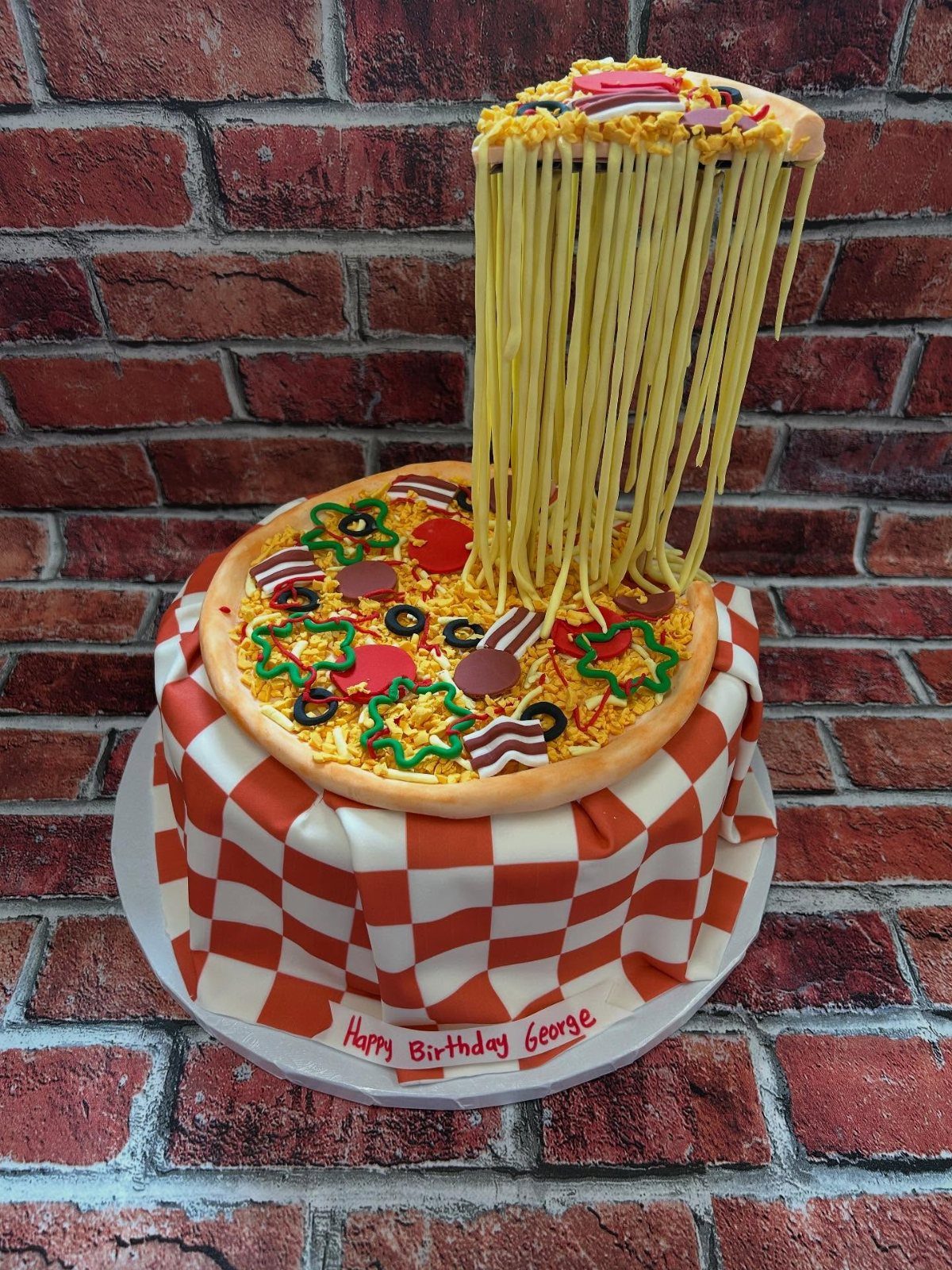 24 Funny Cakes Ideas for Birthdays, From Pizza to Poop Emoji 6 Pizza slice cake with gooey cheese strands lifting a piece against brick wall.