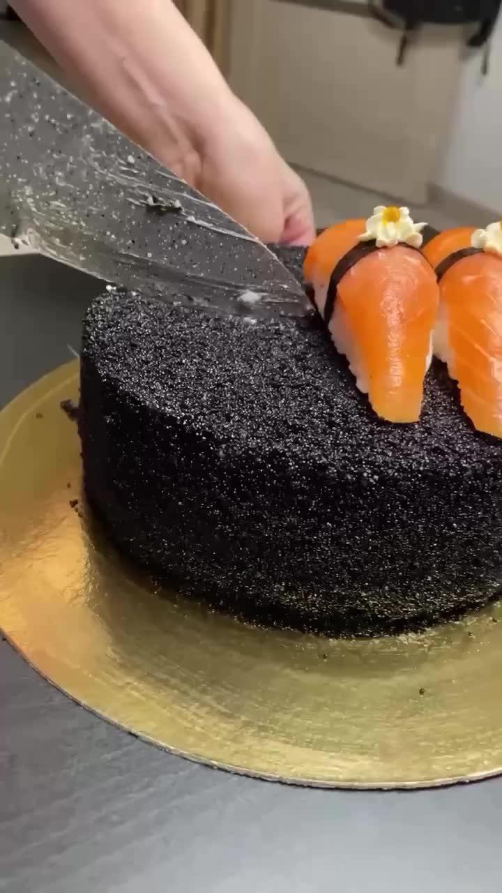 24 Funny Cakes Ideas for Birthdays, From Pizza to Poop Emoji 19 Sushi-shaped cake with black frosting and orange salmon toppings being sliced by a knife.