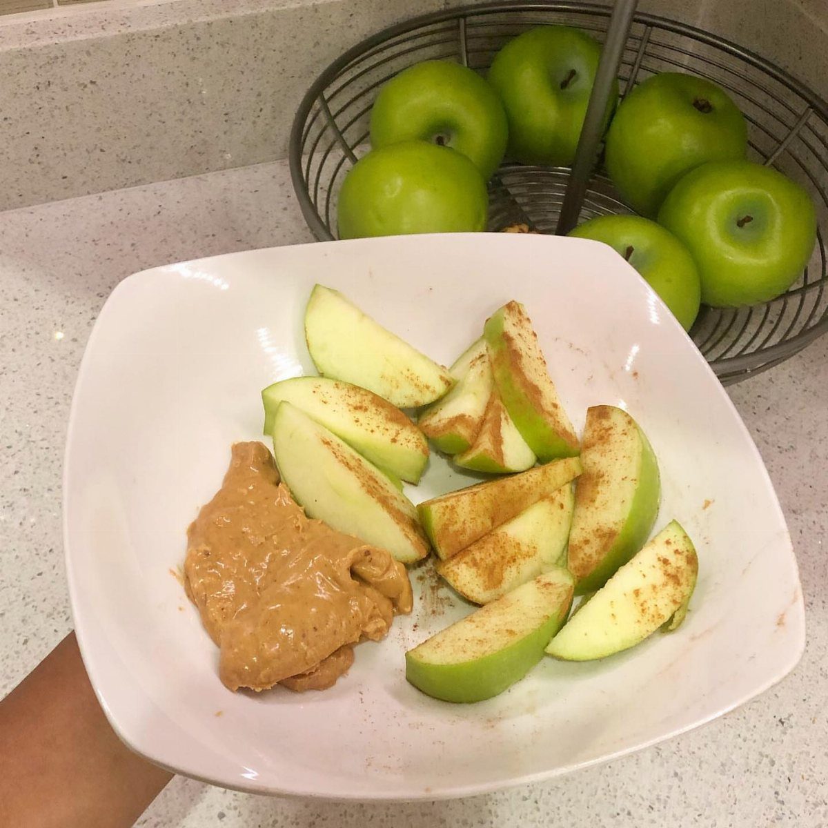 Green apple slices and peanut butter in a white bowl with whole apples behind.