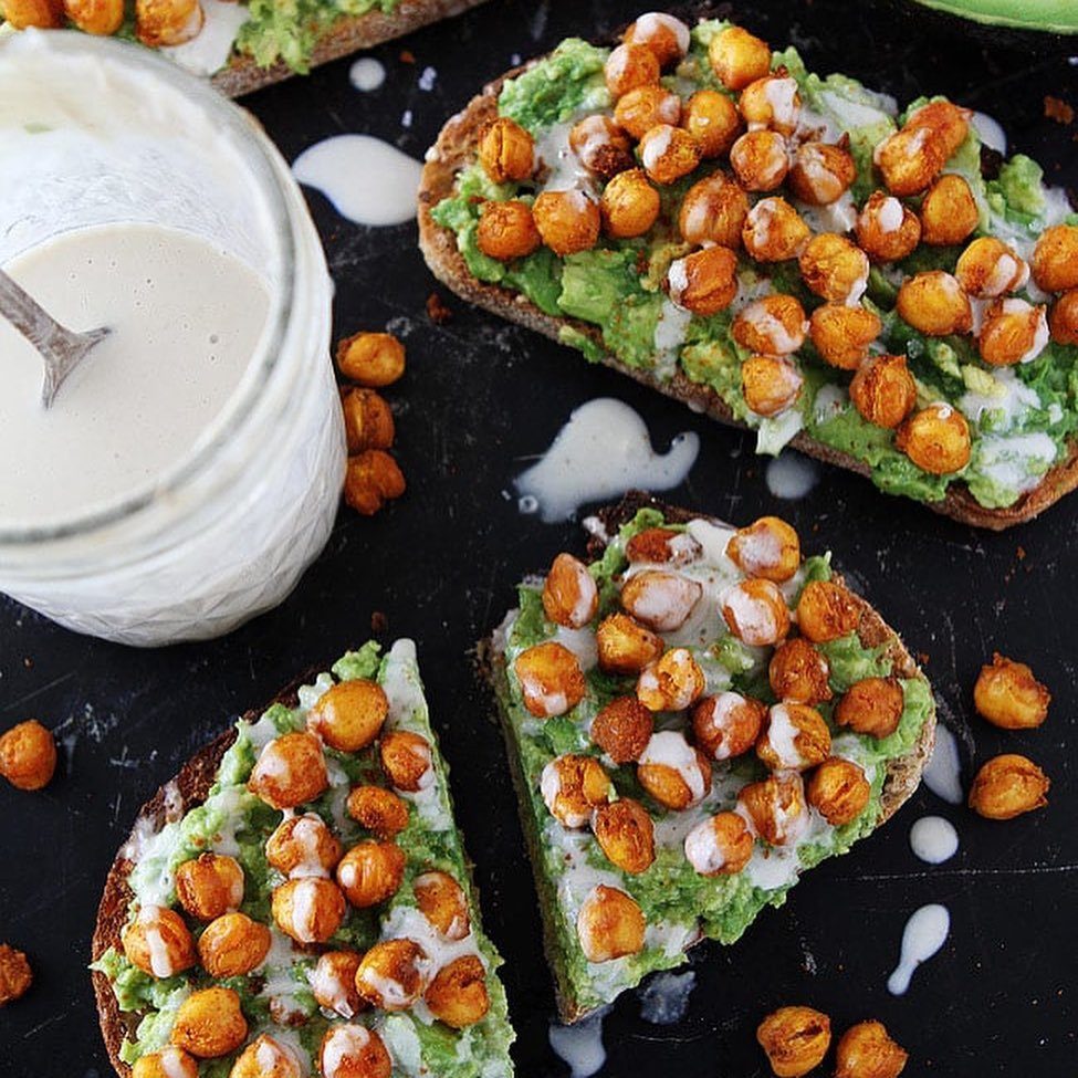 Avocado toast topped with roasted chickpeas and white sauce on a dark background.