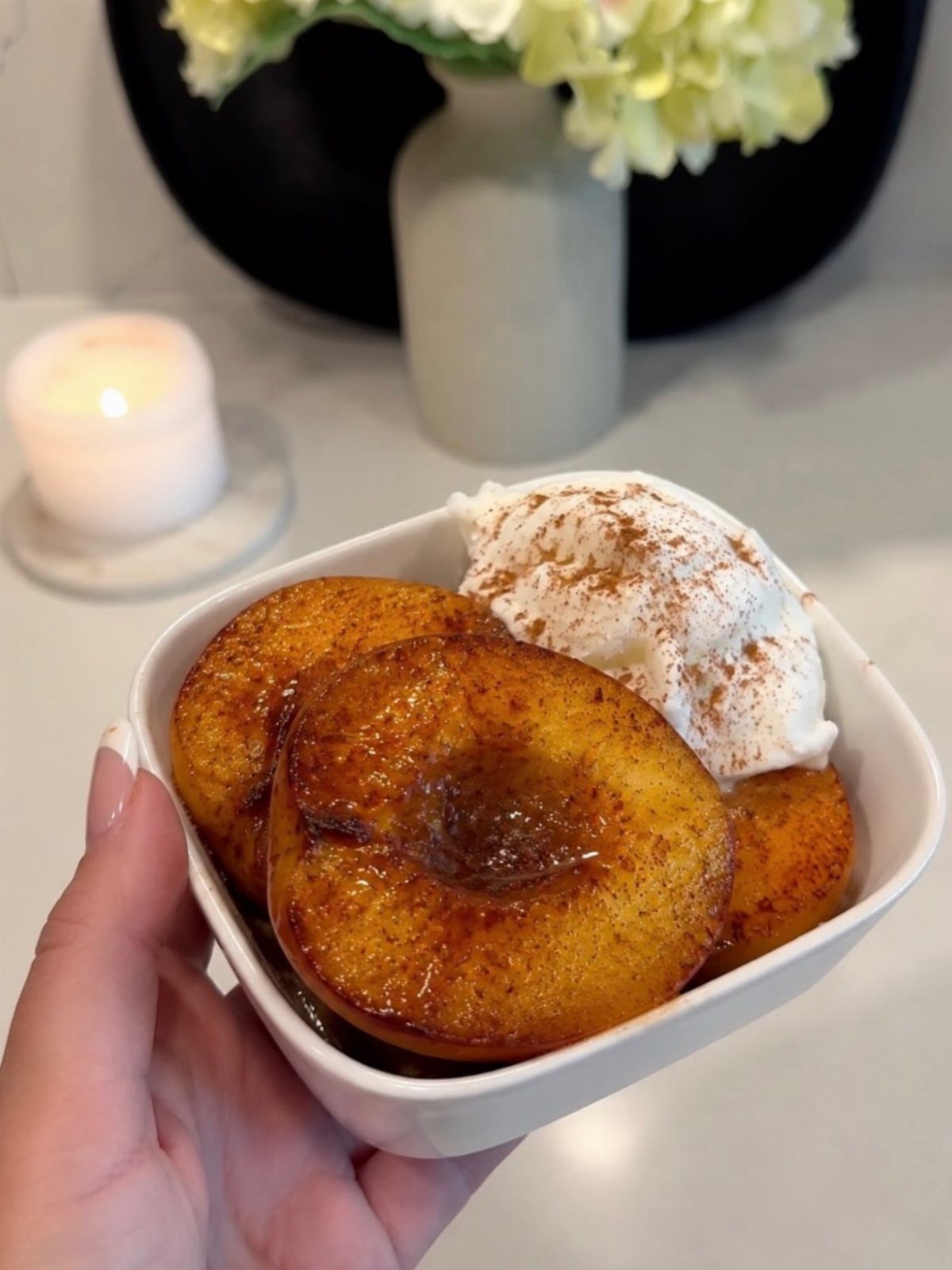 Caramelized peach halves with a dollop of cream in a small white bowl.